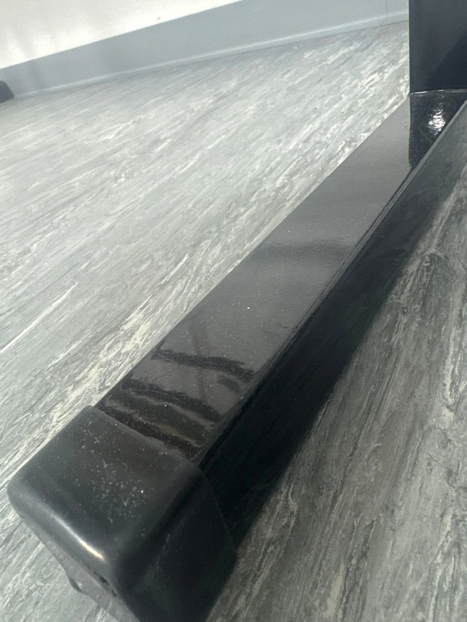 Close-up of a black, glossy, rectangular object placed on a gray, wooden surface with a textured appearance.