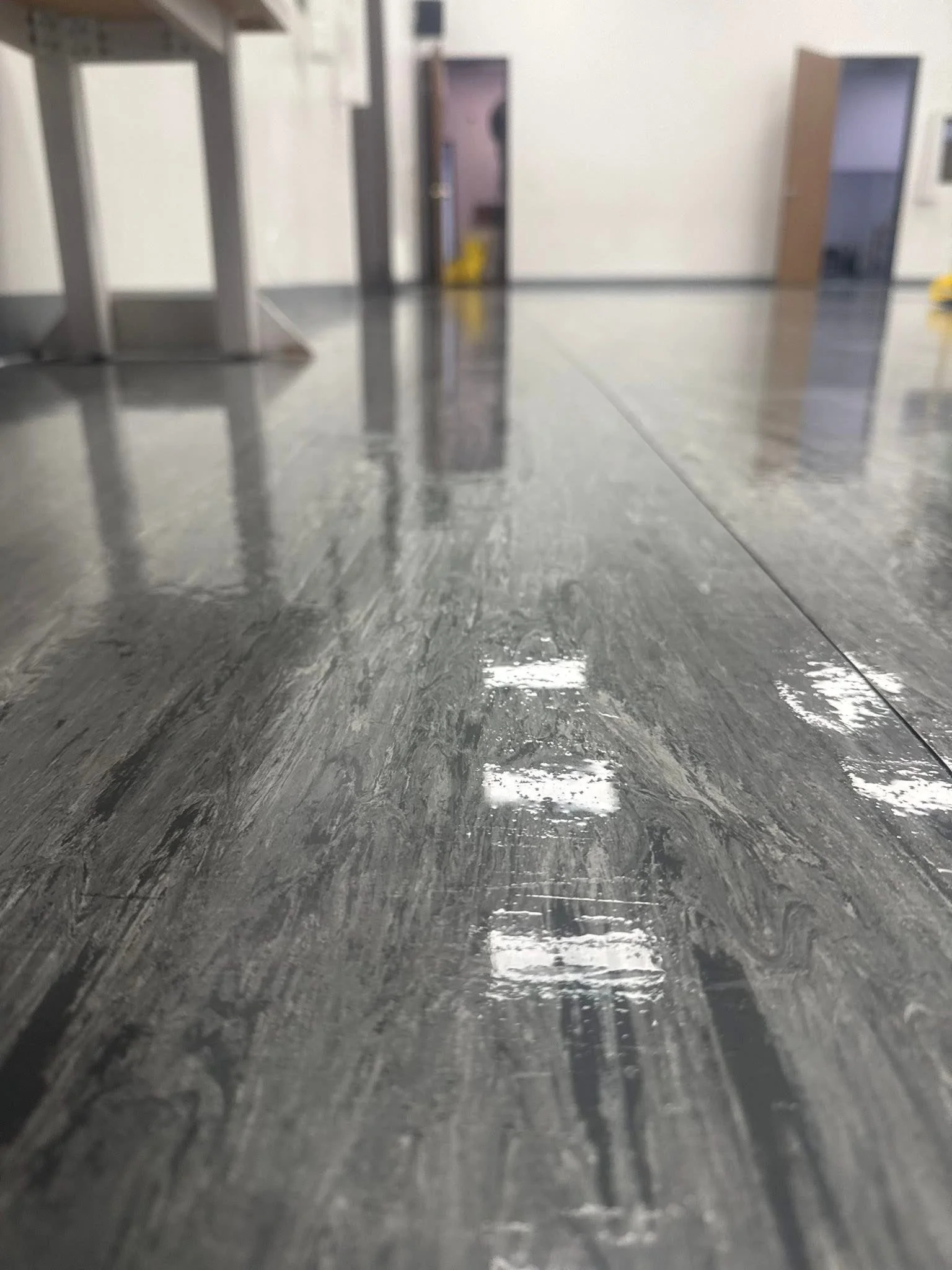 Close-up view of a glossy, gray tile floor in an indoor space, with reflections of the ceiling lights.