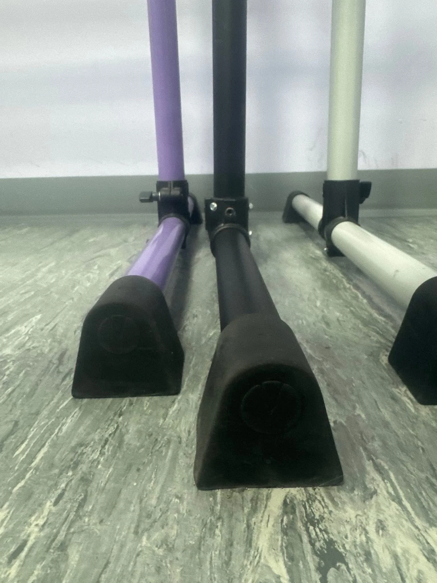 Close-up of three upright hockey sticks with black padded blades resting on a grayish floor.