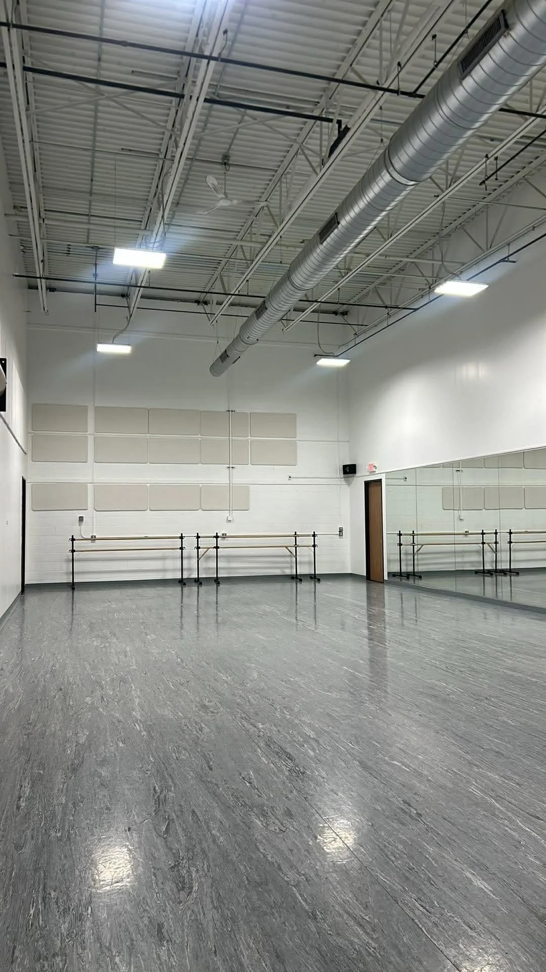 Empty dance studio with mirrored wall, ballet barres, and ceiling fans.