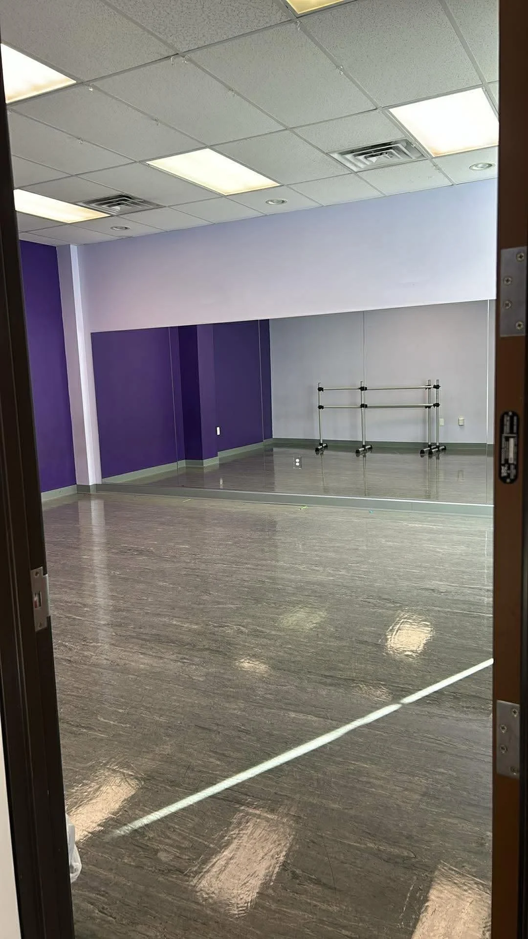 Empty dance studio with purple and gray walls, a large mirror, and ballet barres.