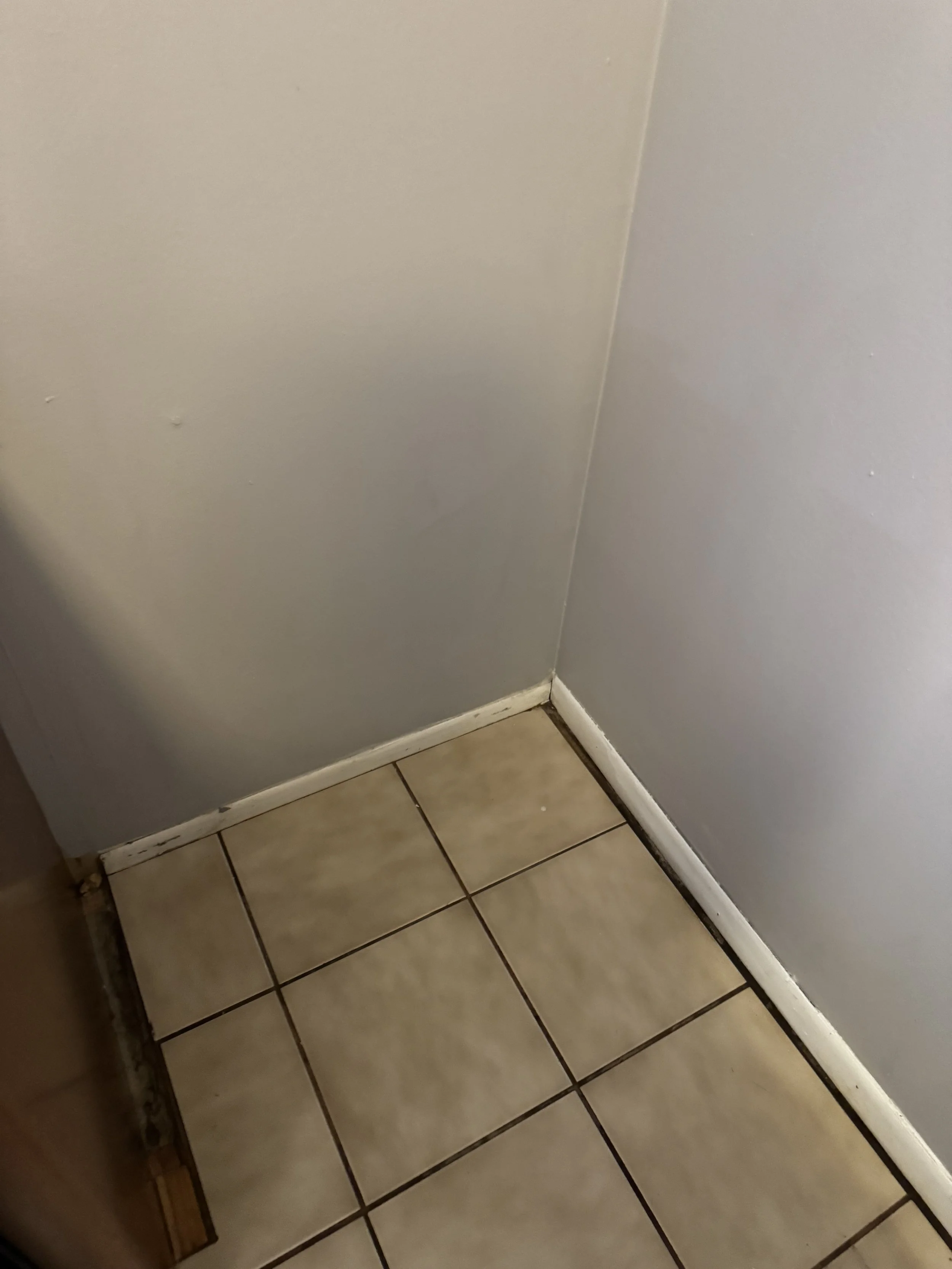 Corner of a room showing beige tiled floor, white baseboard molding, and gray painted walls.