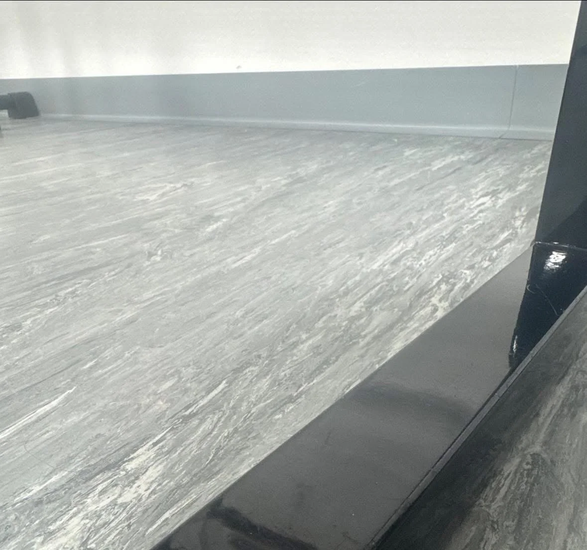Close-up of a countertop with a gray, marble-like pattern, and a black edge on the bottom right.