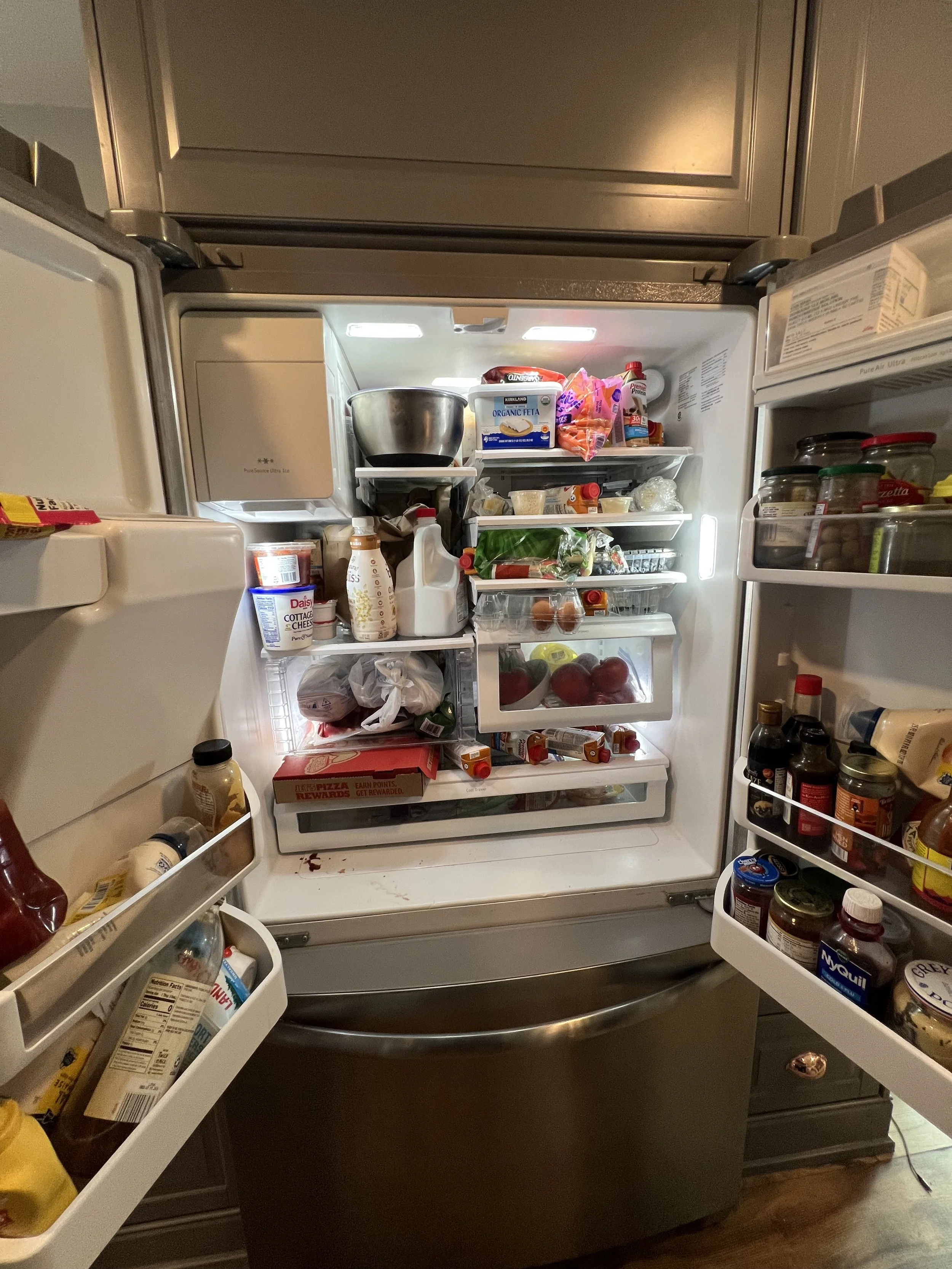 Open refrigerator with various food items, fruits, vegetables, condiments, and beverages inside.