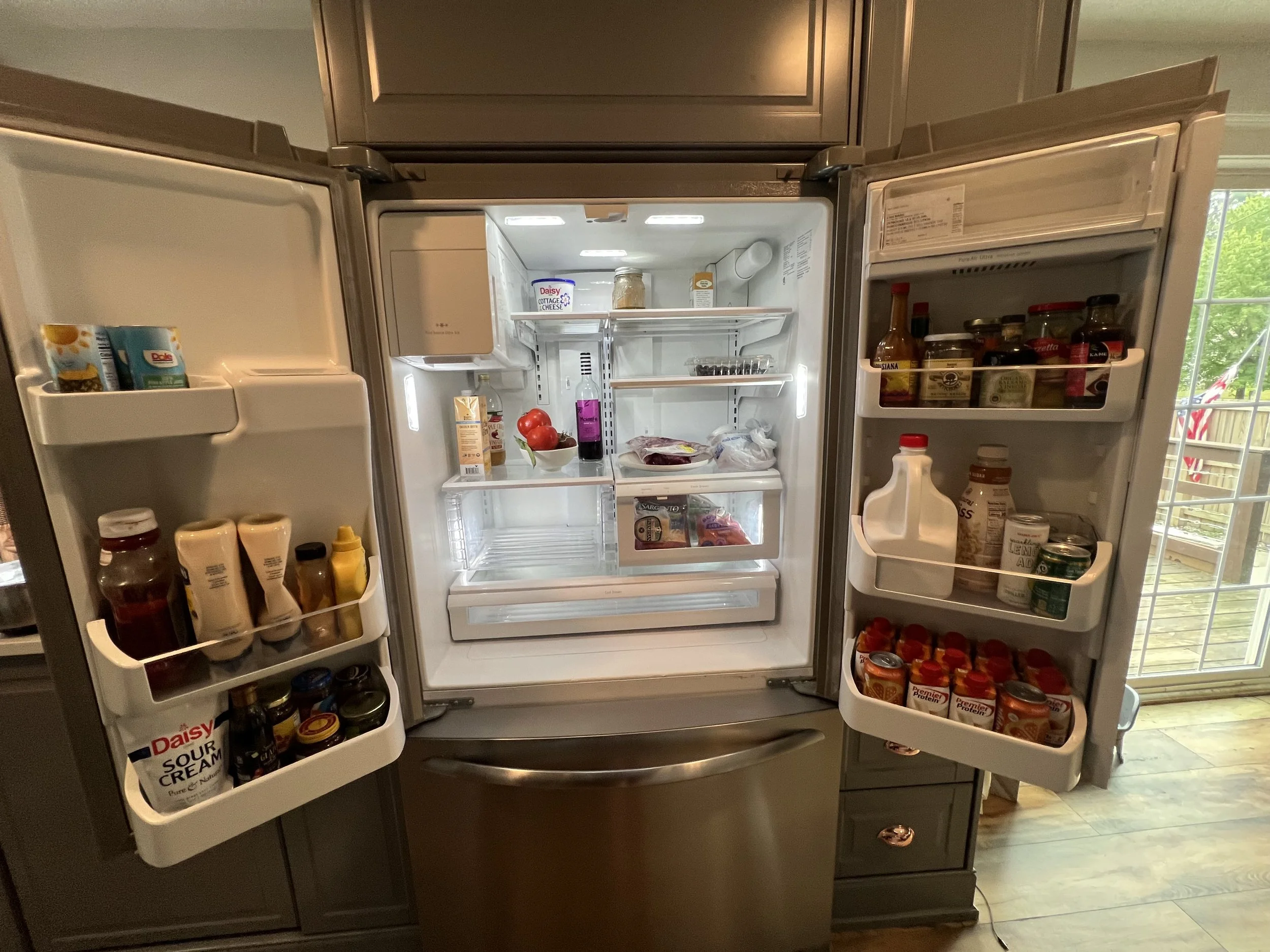 Open refrigerator with various food and condiments on the shelves and door, including tomatoes, yogurt, mustard, ketchup, sauces, and jars of spices.