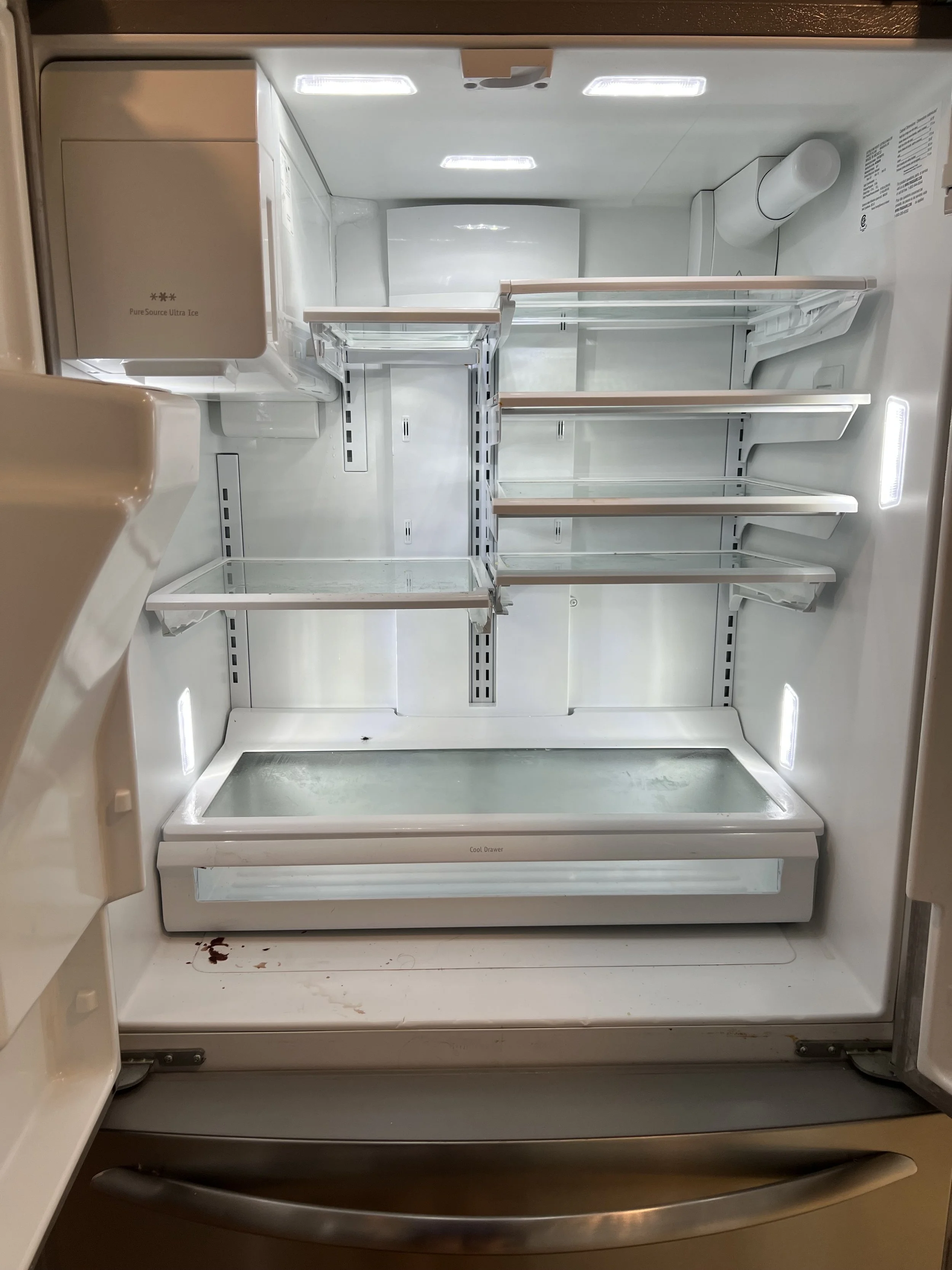 Empty refrigerator with a few stains on the bottom shelf, and bright interior lights.