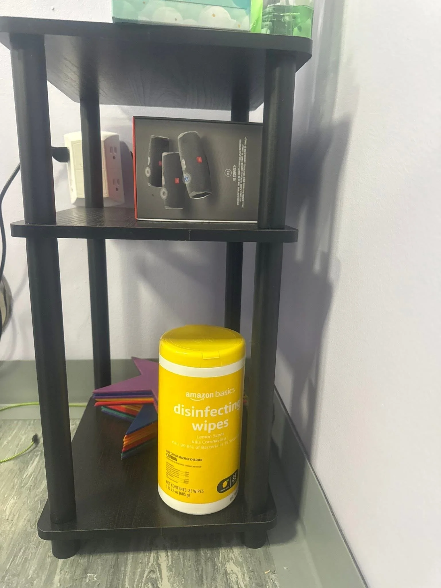 Shelf with Amazon disinfecting wipes container, colorful star-shaped objects, and a box of wireless earbuds.