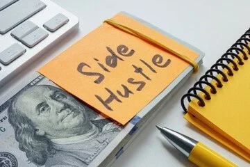 Close-up of a workspace with a dollar bill, a yellow notepad, and a sticky note labeled 'Side Hustle' SIDE HUSTLE TAX RETURN