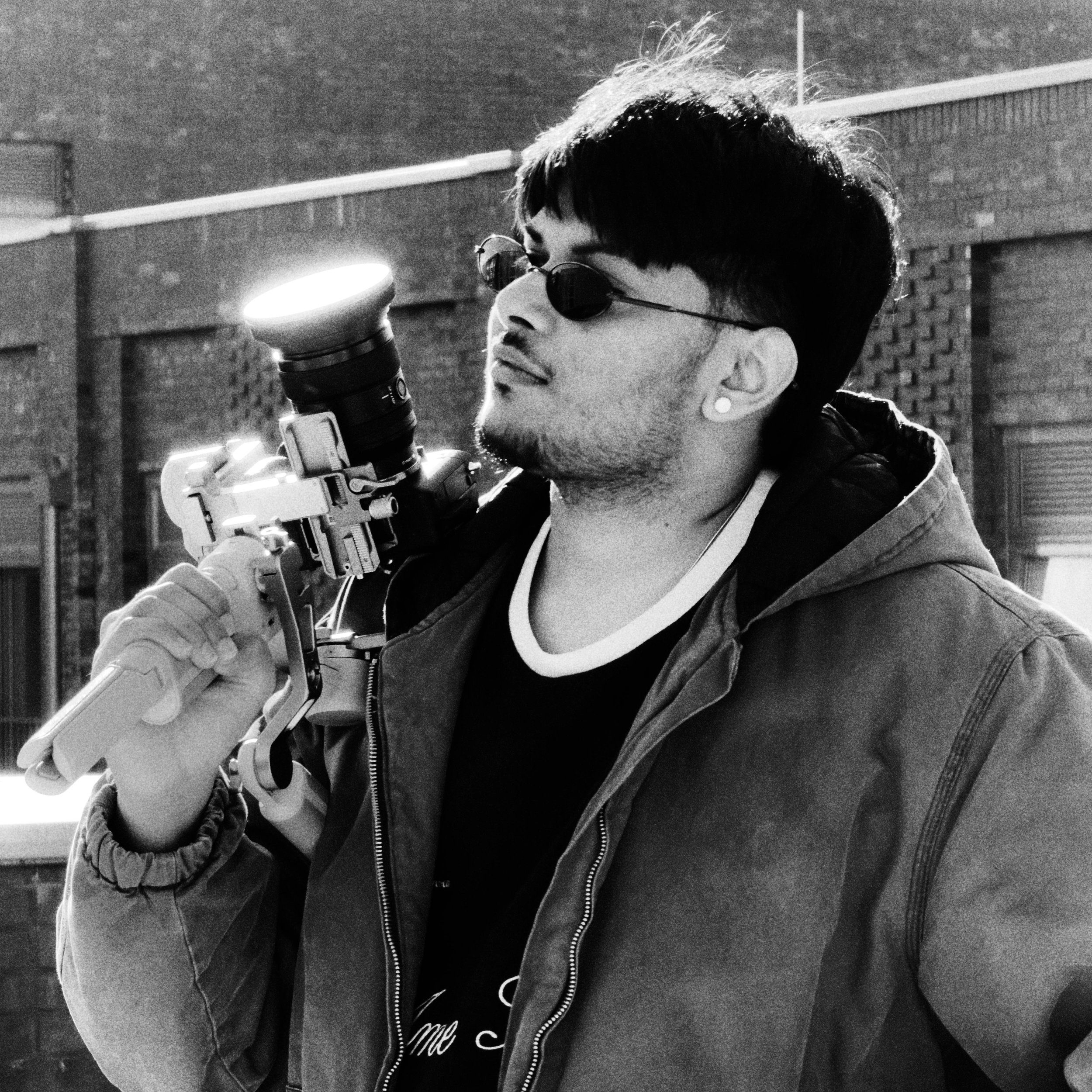 Black and white portrait of a person holding up a camera against his shoulder. Casual expression