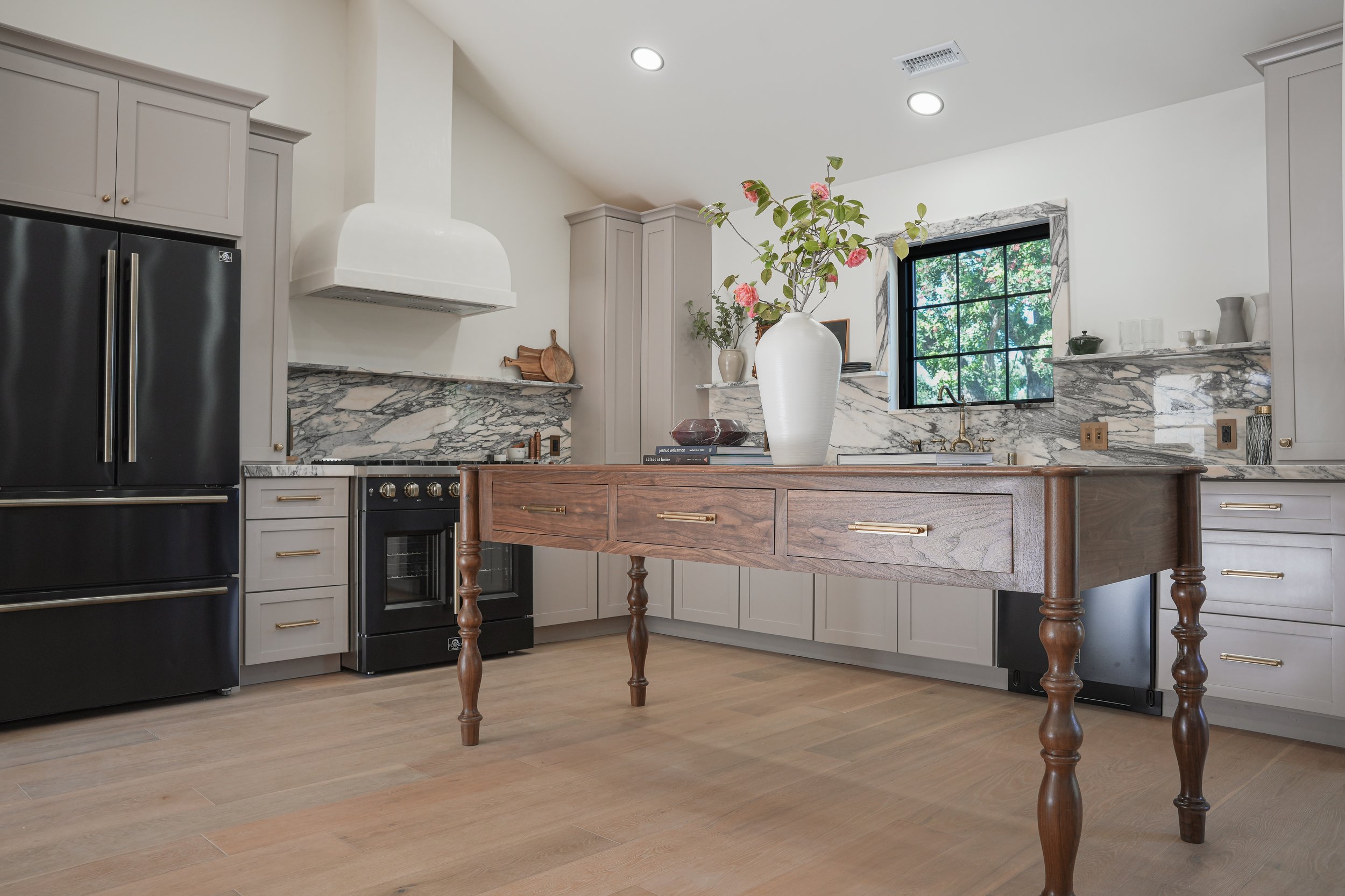 3D rendering of a modern kitchen with black appliances, white cabinetry, a wooden table, and a window on the wall.