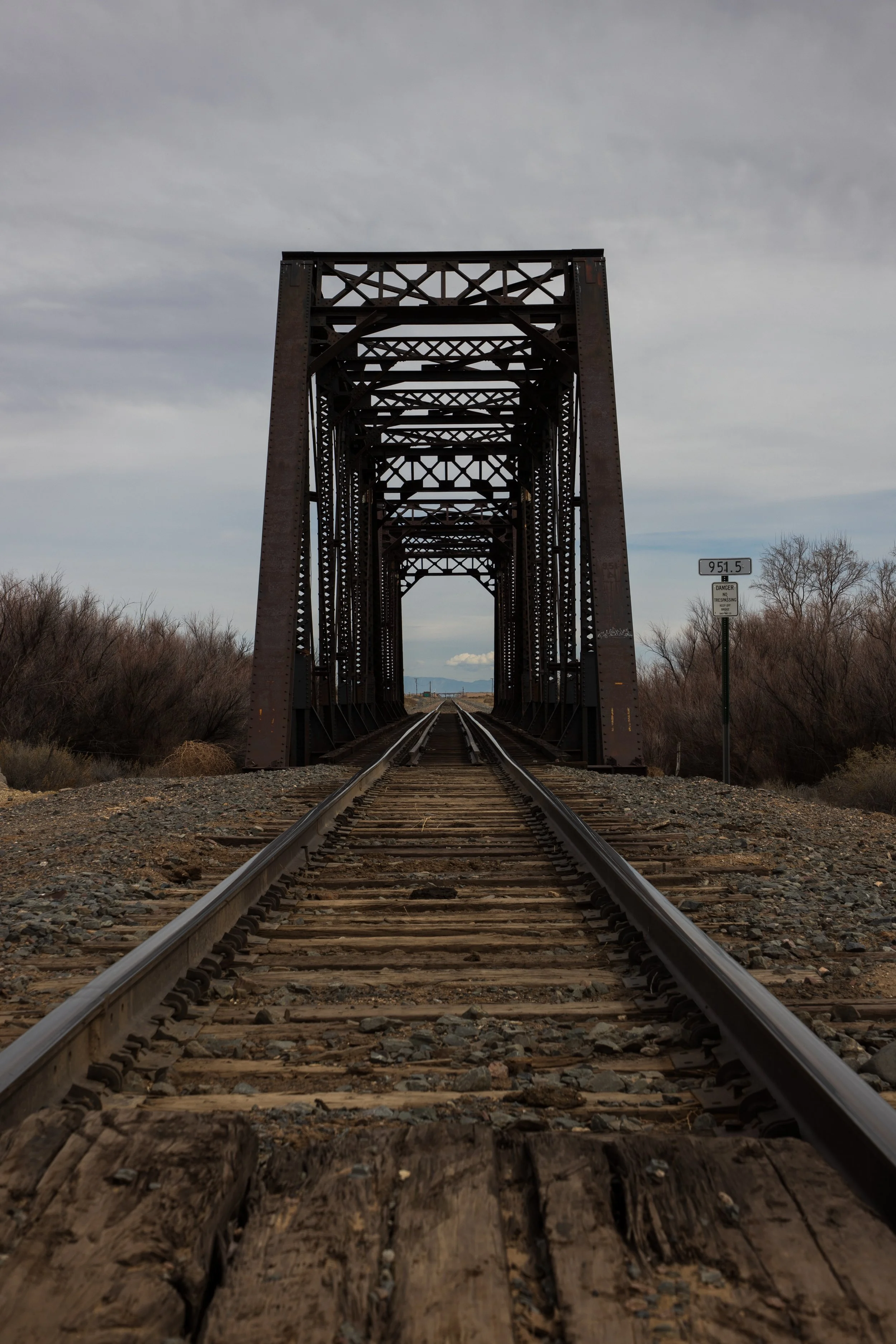 Railroad bridge with metal trusses over a gravel railway track.