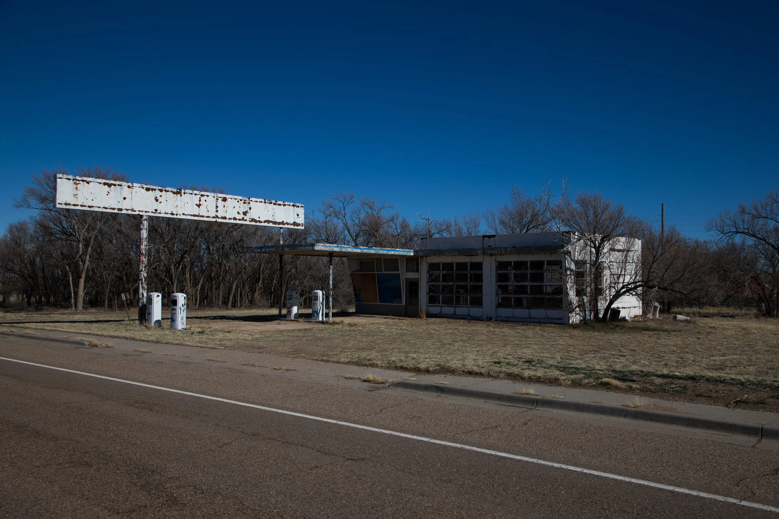 Abandoned vintage gas station with rusty signage and old gas pumps on a deserted road.