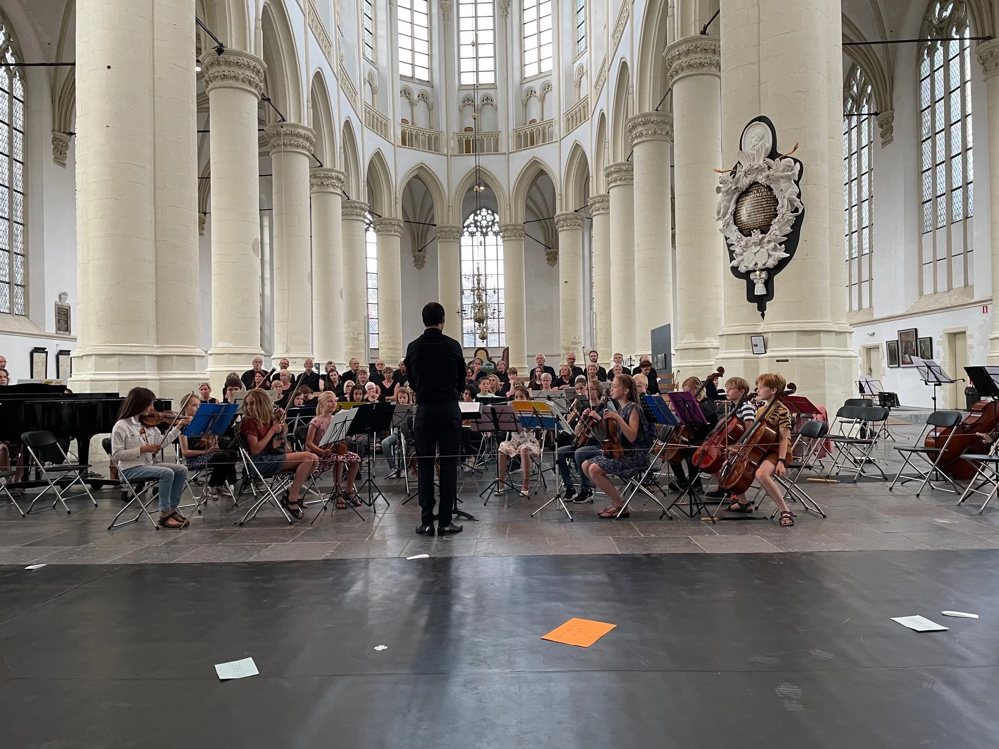 Choir and orchestra rehearsal in a cathedral with a conductor leading the musicians.