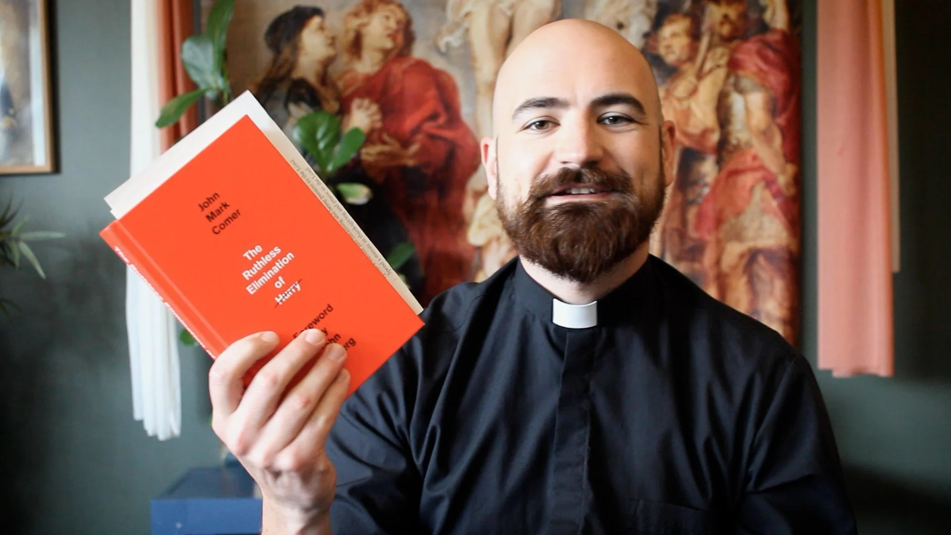 Screenshot from a video of a priest holding up the book he is discussing, which is The Ruthless Elimination of Hurry by John Mark Comer