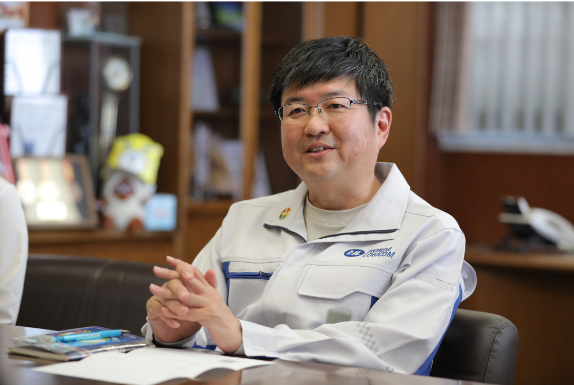 A man in a light blue work uniform and glasses smiling indoors.