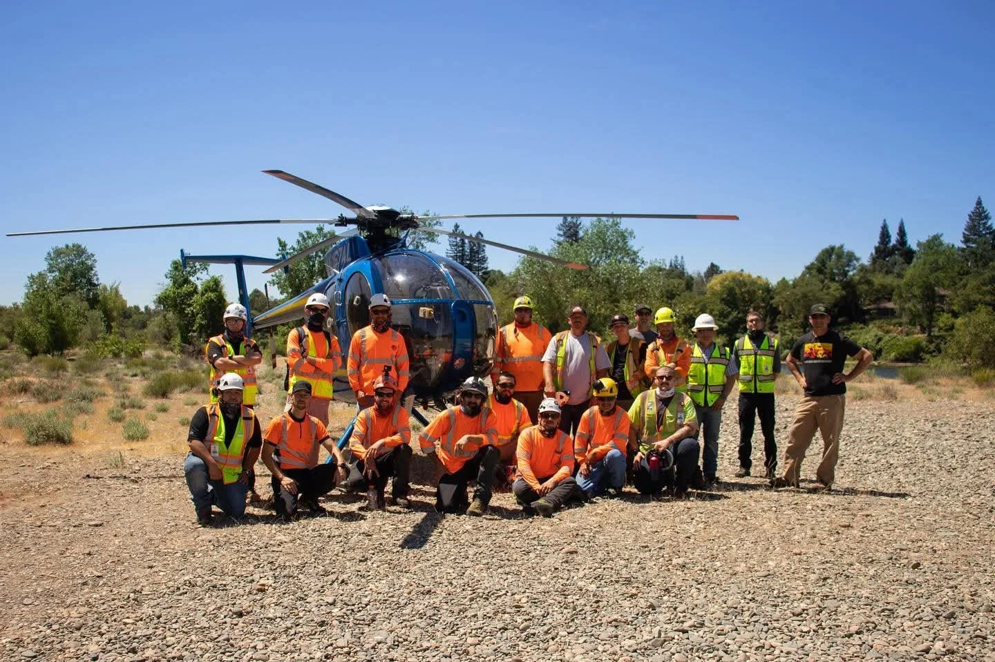 Group of people in safety vests and helmets standing in front of a helicopter outdoors on a sunny day.