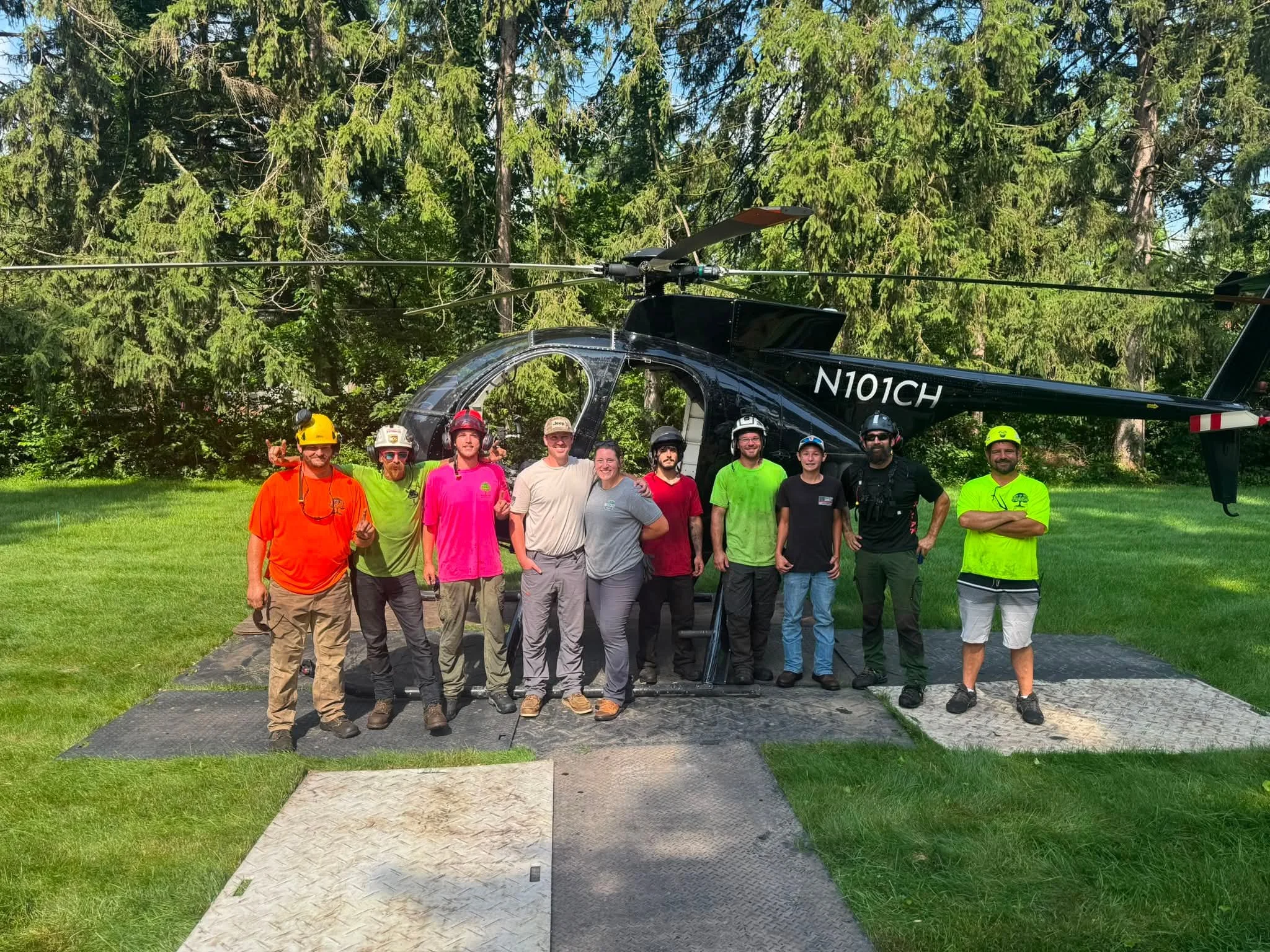 Group of people in safety helmets and casual wear, standing in front of a helicopter outdoors.