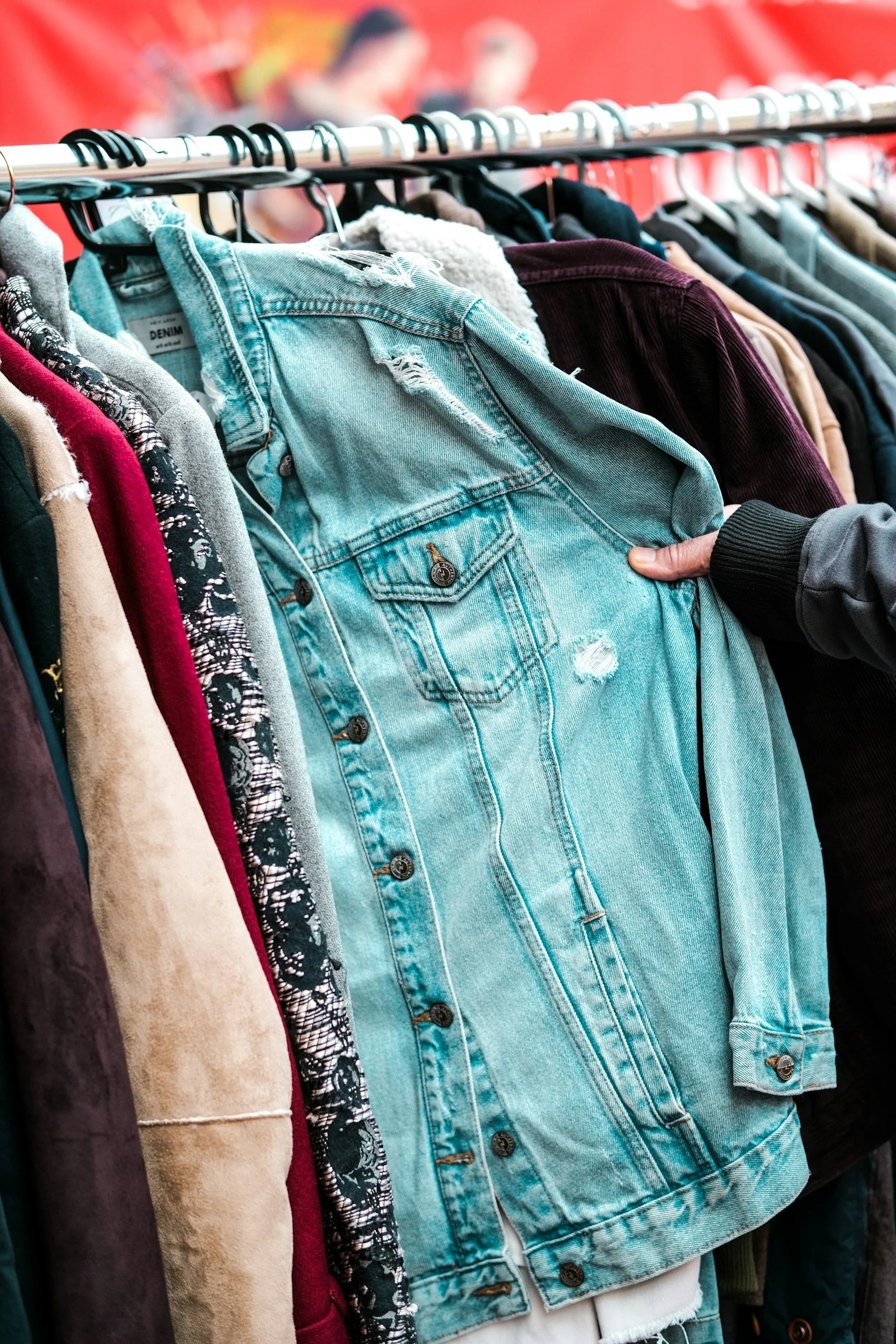 A row of various jackets and shirts hanging on a rack at a thrift store, including denim, corduroy, and patterned fabrics.