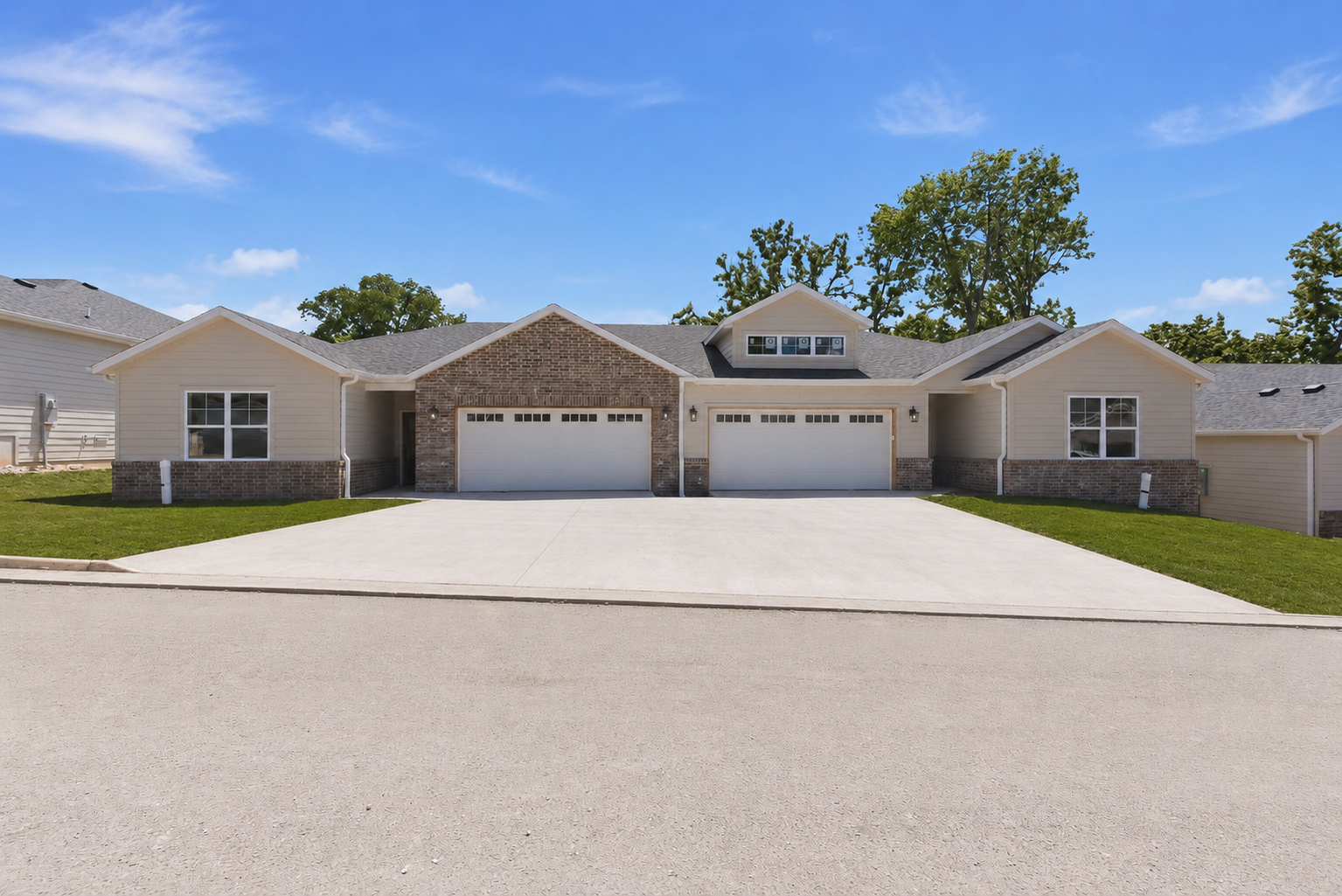 Front view of a residential house with a newly paved driveway, brick and vinyl siding, a gable roof, and landscaping in progress with bare dirt in the yard.