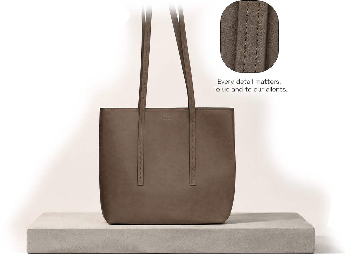 A brown leather tote bag with long handles displayed on a white surface against a white background, with a close-up detail of the stitching and texture.