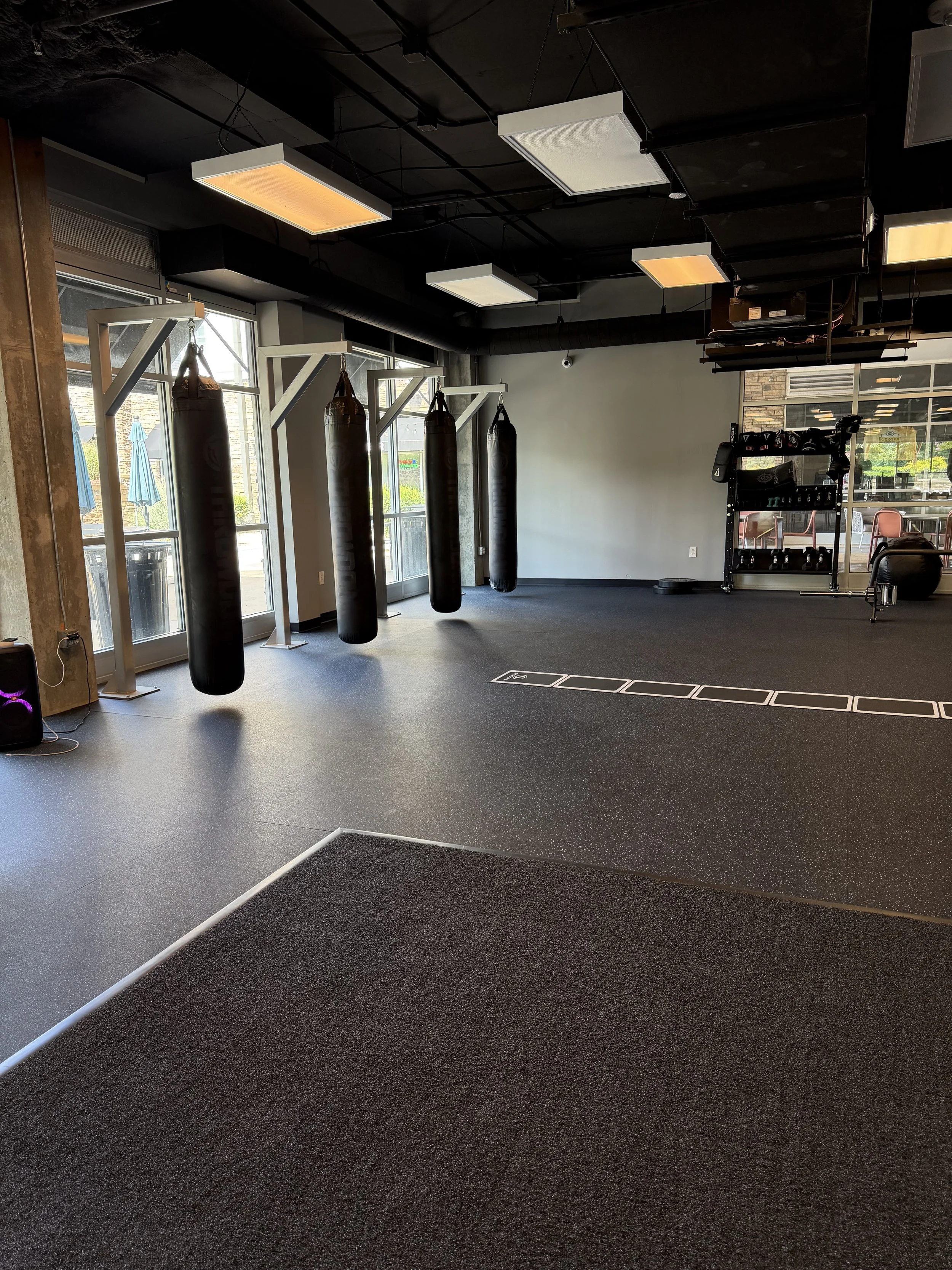 Empty fitness gym with punching bags, weight rack, and open windows.