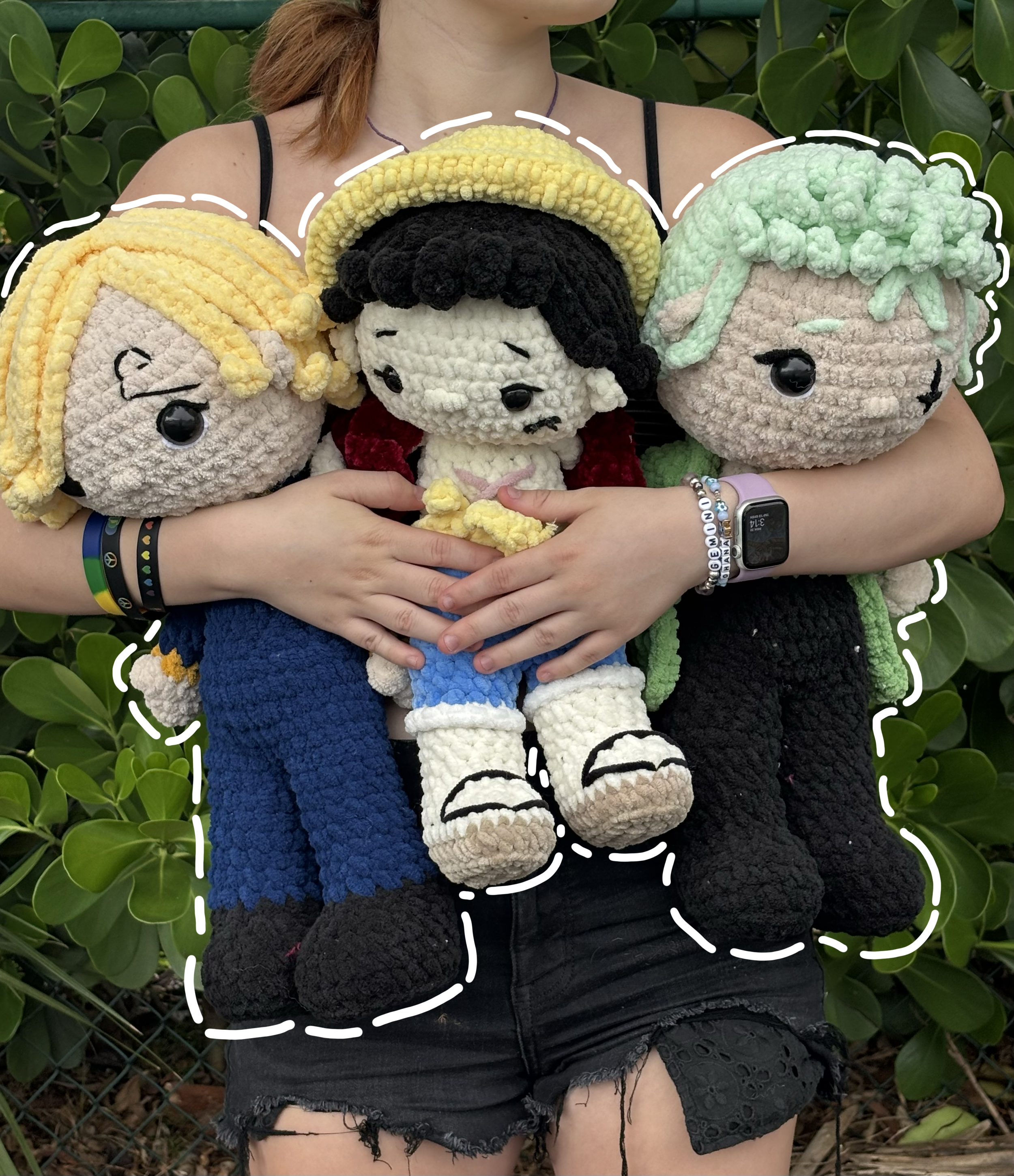 Person holding handmade crochet plushies of One Piece characters, Luffy, Zoro, and Sanji. The monster trio.