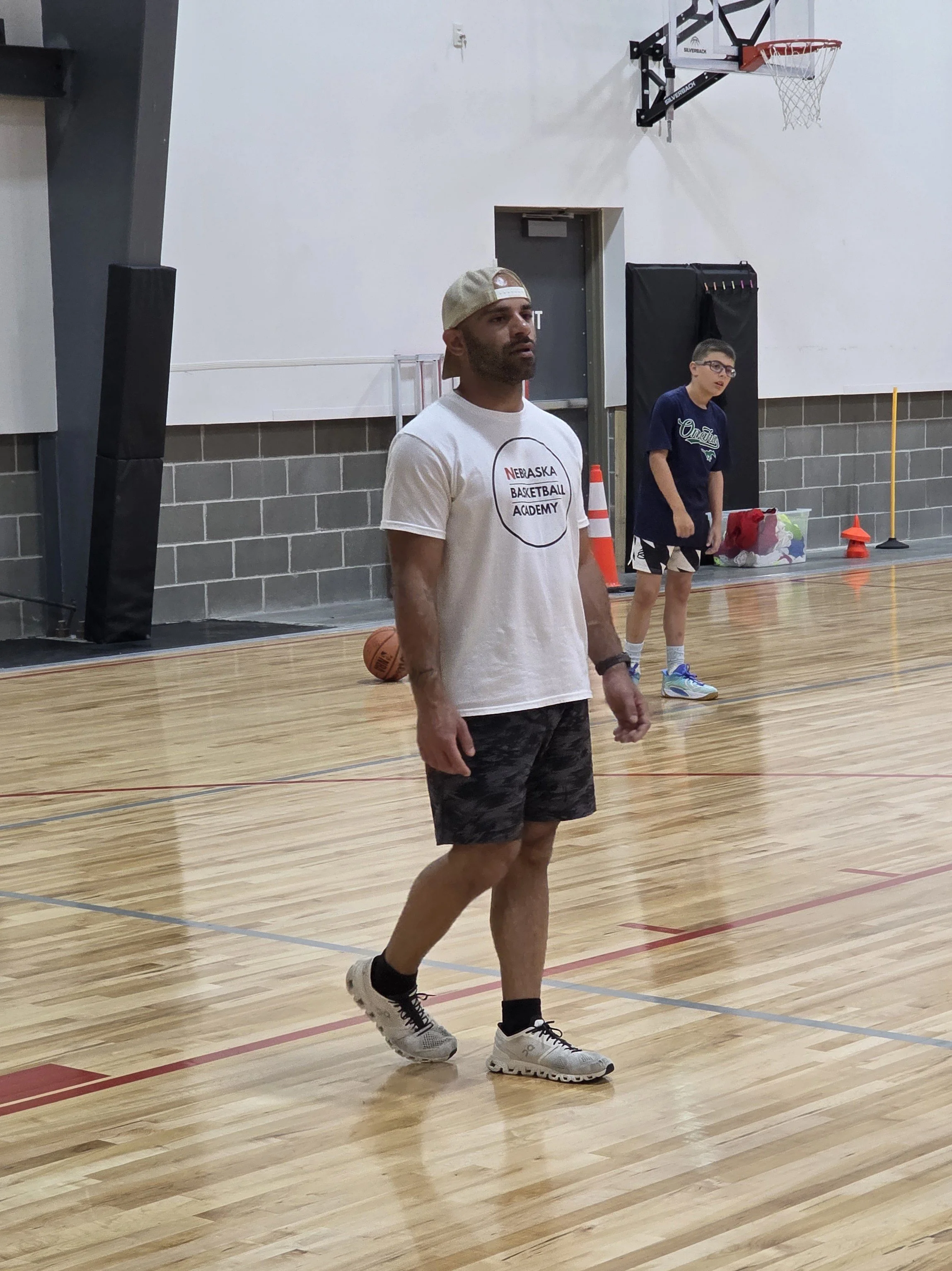 Man in white Nebraska Basketball Academy shirt coaching on a basketball court