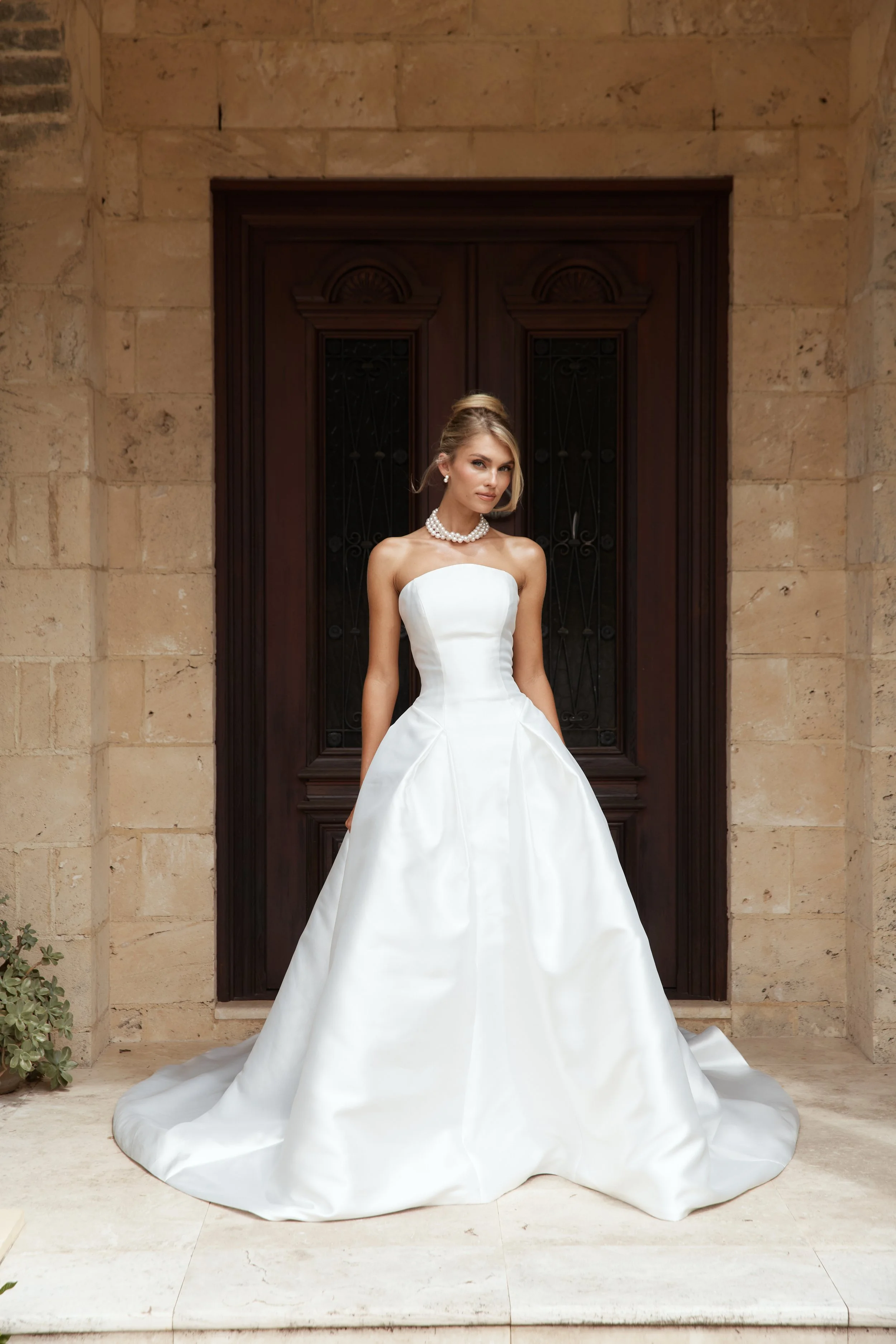A modern bride, in a strapless white wedding gown standing posing for her wedding photos at a hill country estate.