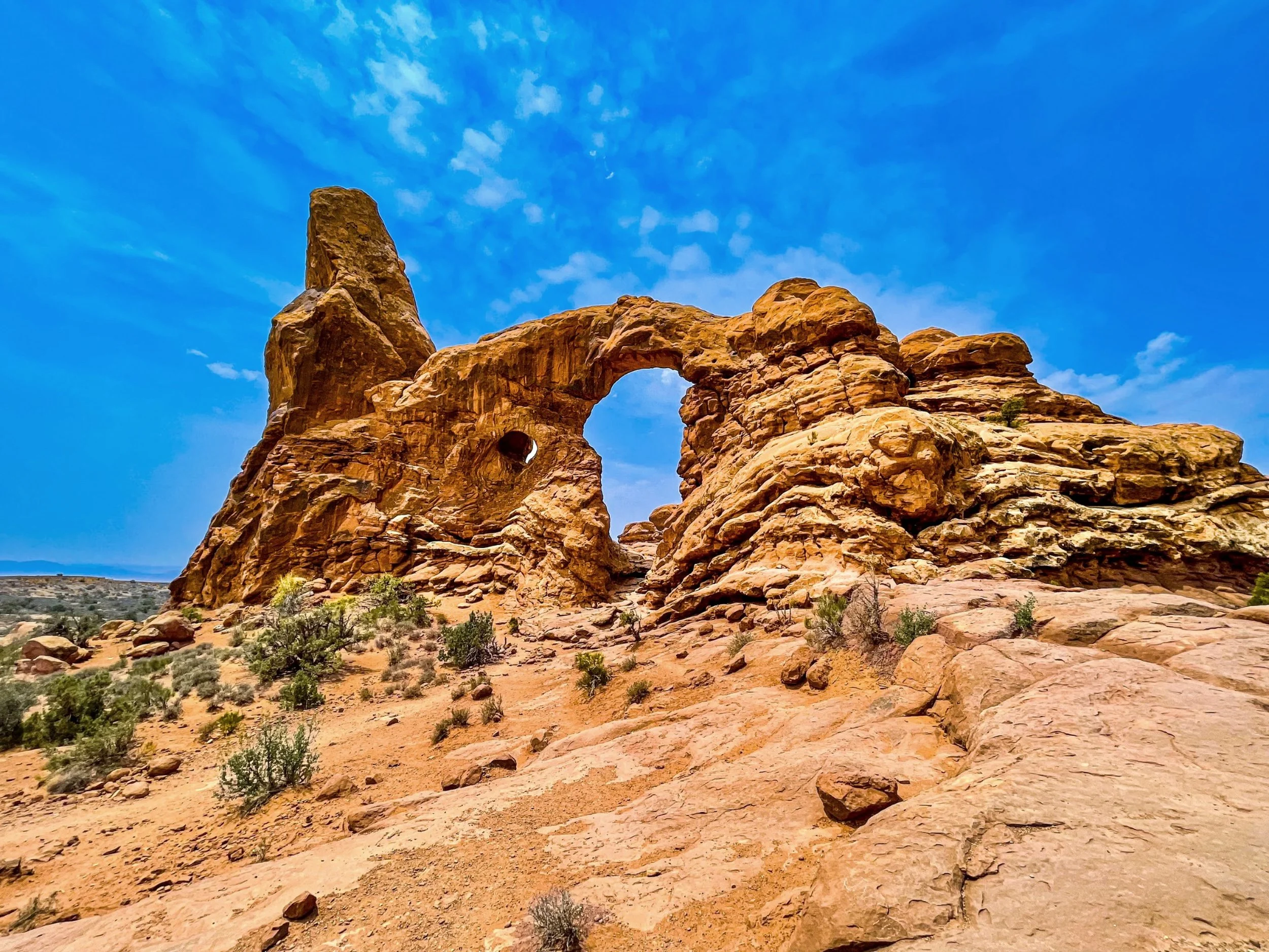 Weathered sandstone arch beside a tall rock spire beneath blue sky
