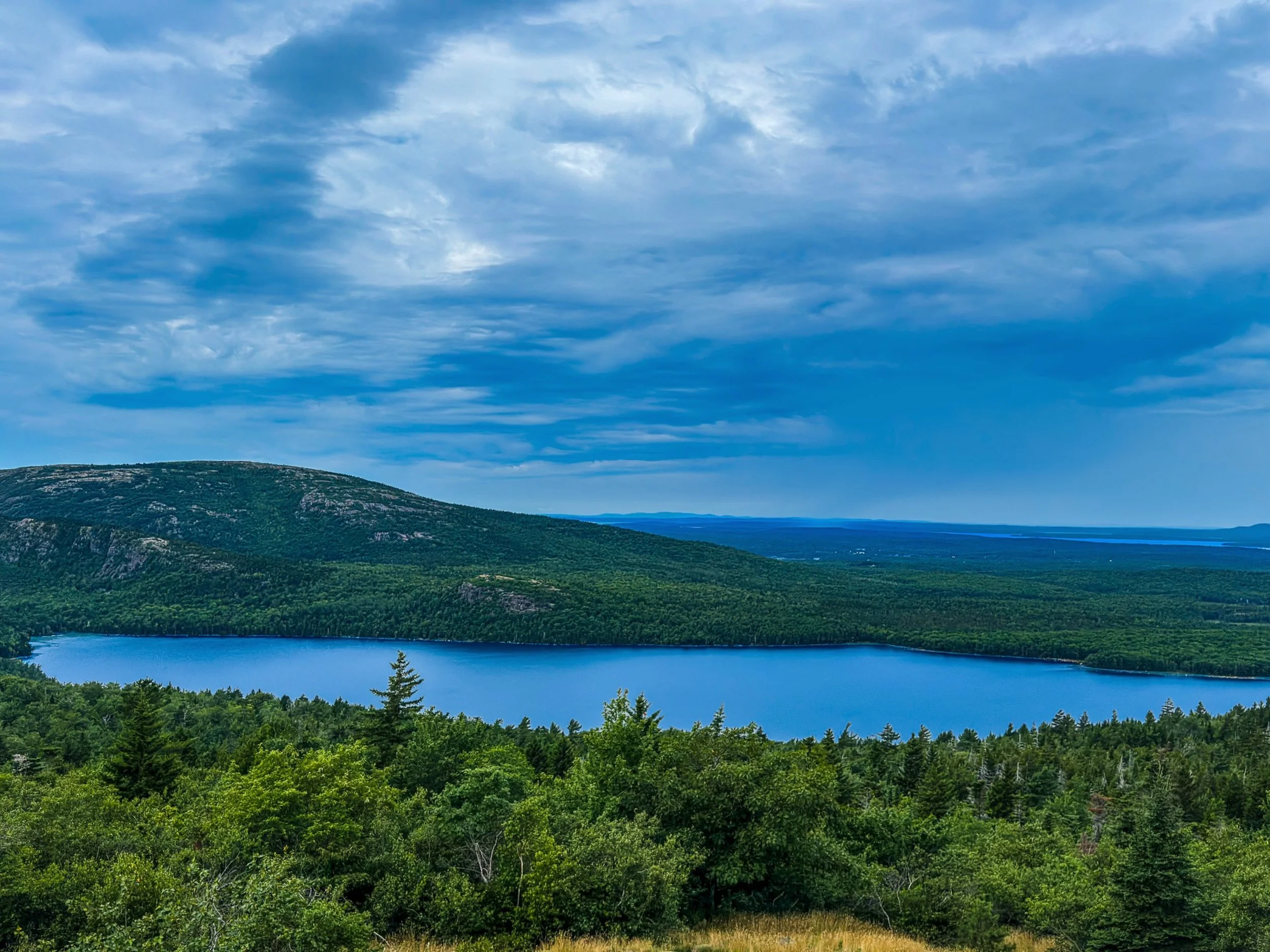 Blue lake surrounded by green forest and low mountains beneath layered clouds