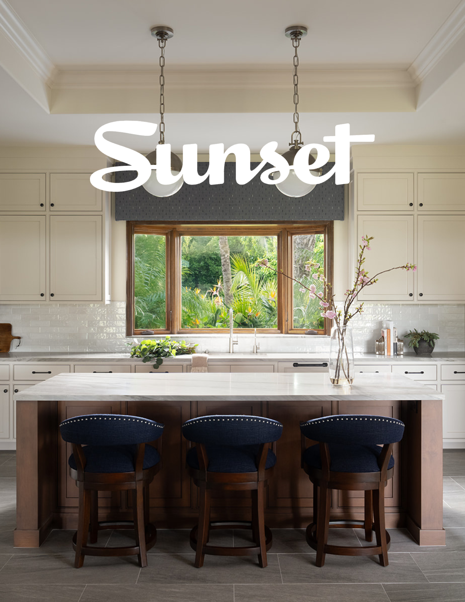 Andrea Lackie design featured in Sunset magazine. Bright remodeled transitional kitchen with off-white painted cabinets, stone countertops, and custom furniture stools. Large window with a garden view and hanging light fixtures in California.