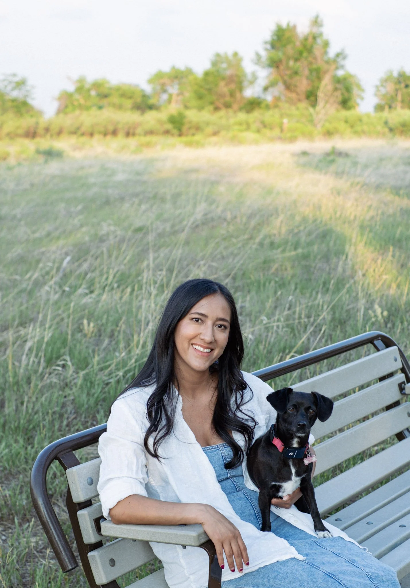 Dominique and Olive smile at the camera while they rest on a bench in front of a lush green meadow.