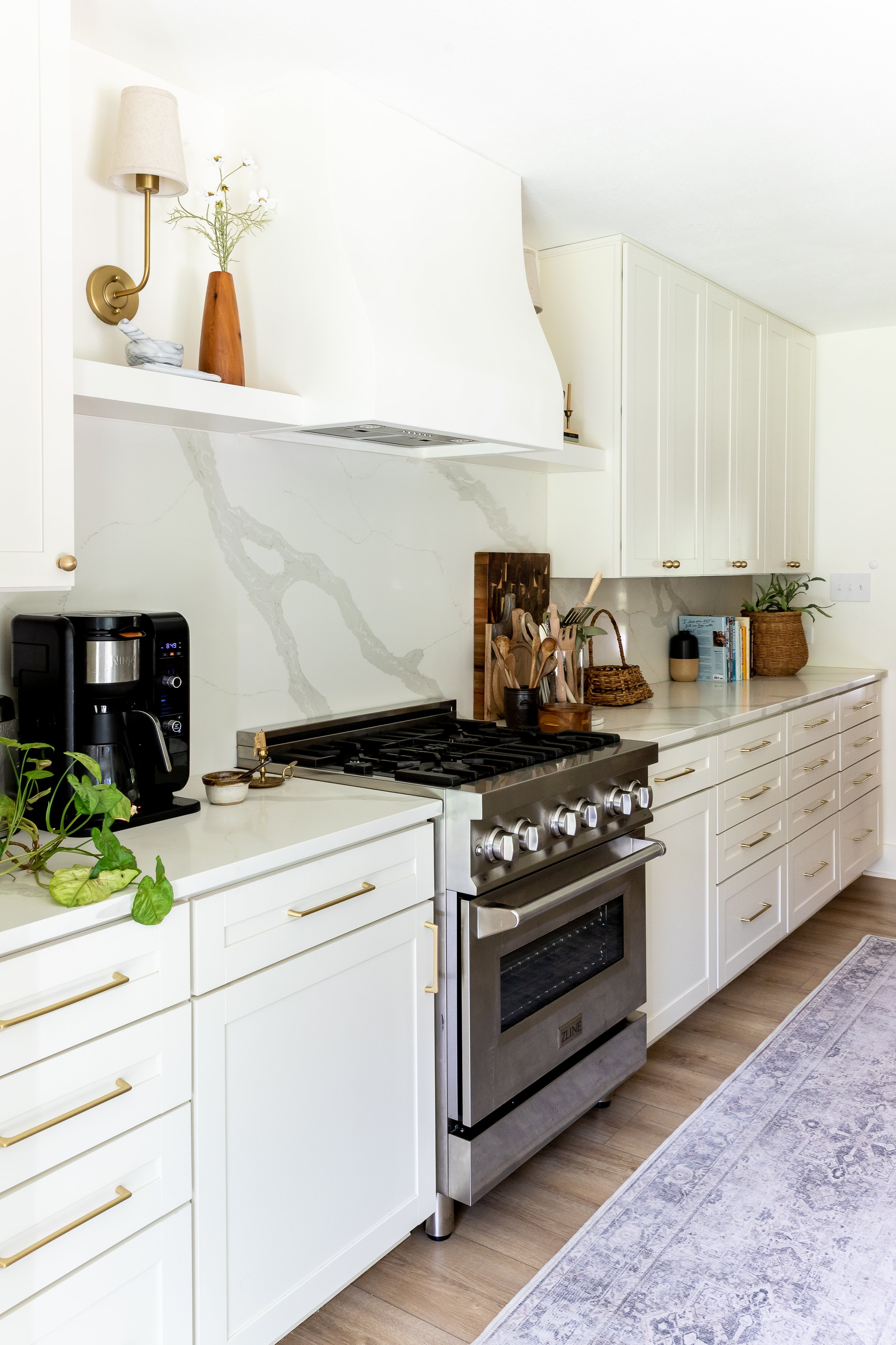 Modern kitchen with white cabinets, marble backsplash, stainless steel stove, coffee maker, and decorative items on the counter.