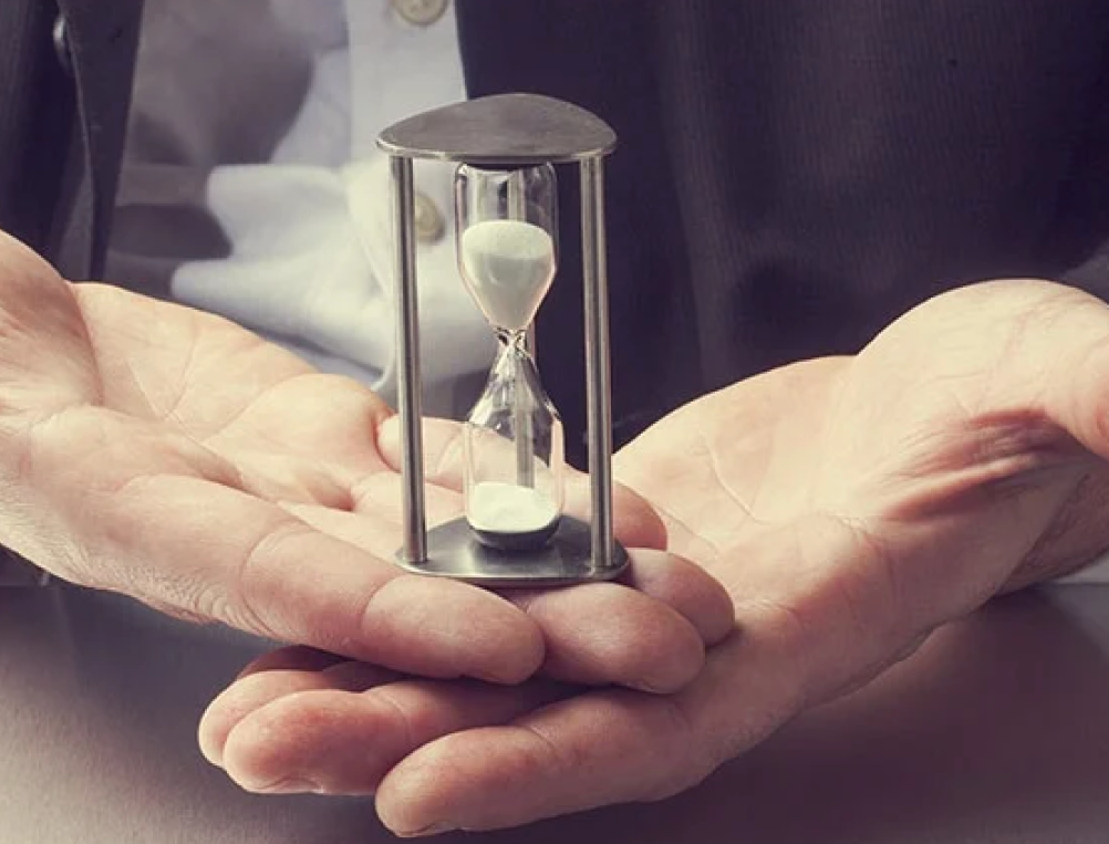 Person holding a small hourglass with white sand inside.
