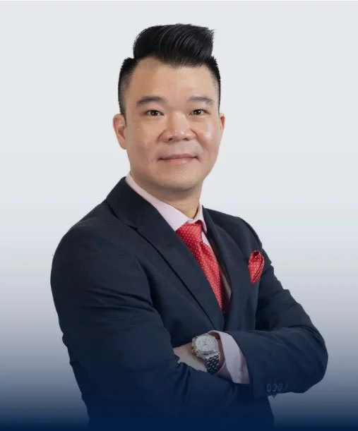 Professional man in a dark suit with a red tie and pocket square, crossing his arms against a light gradient background.
