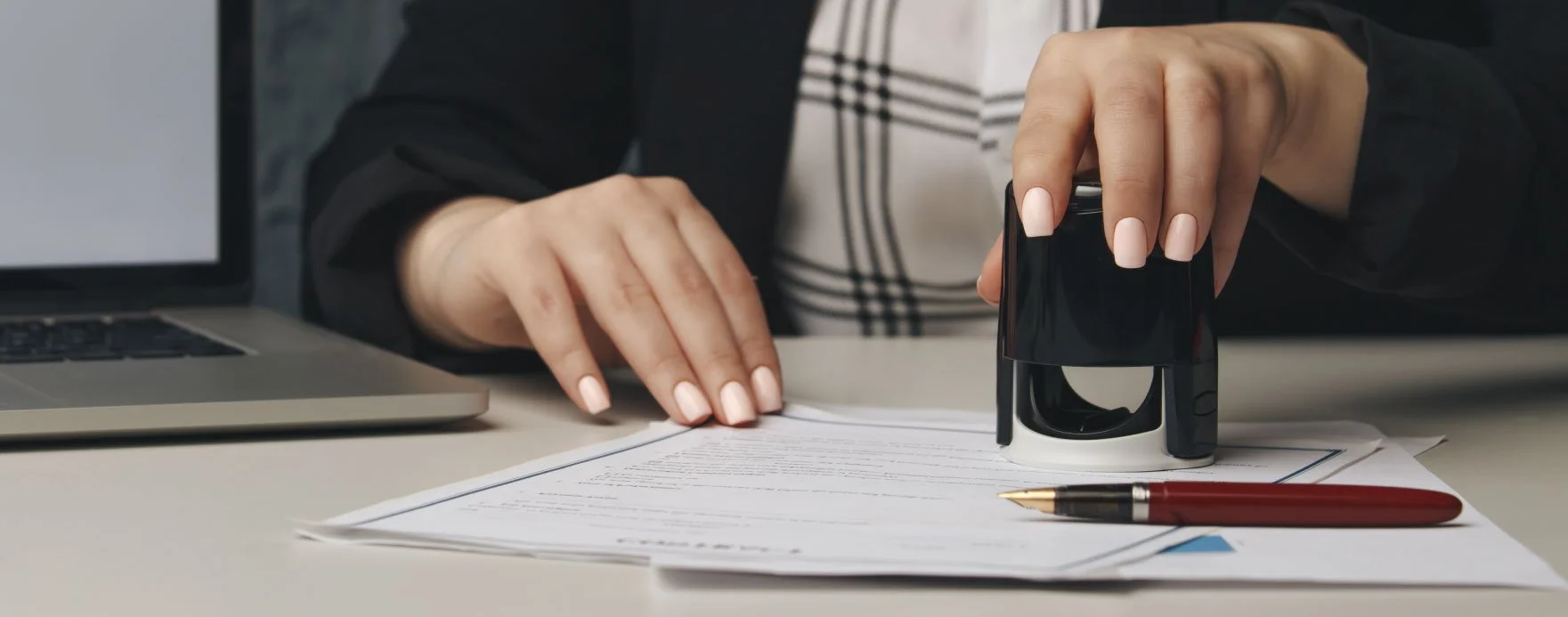 Person stamping a document with a self-inking stamp on a desk with a laptop and a red pen.