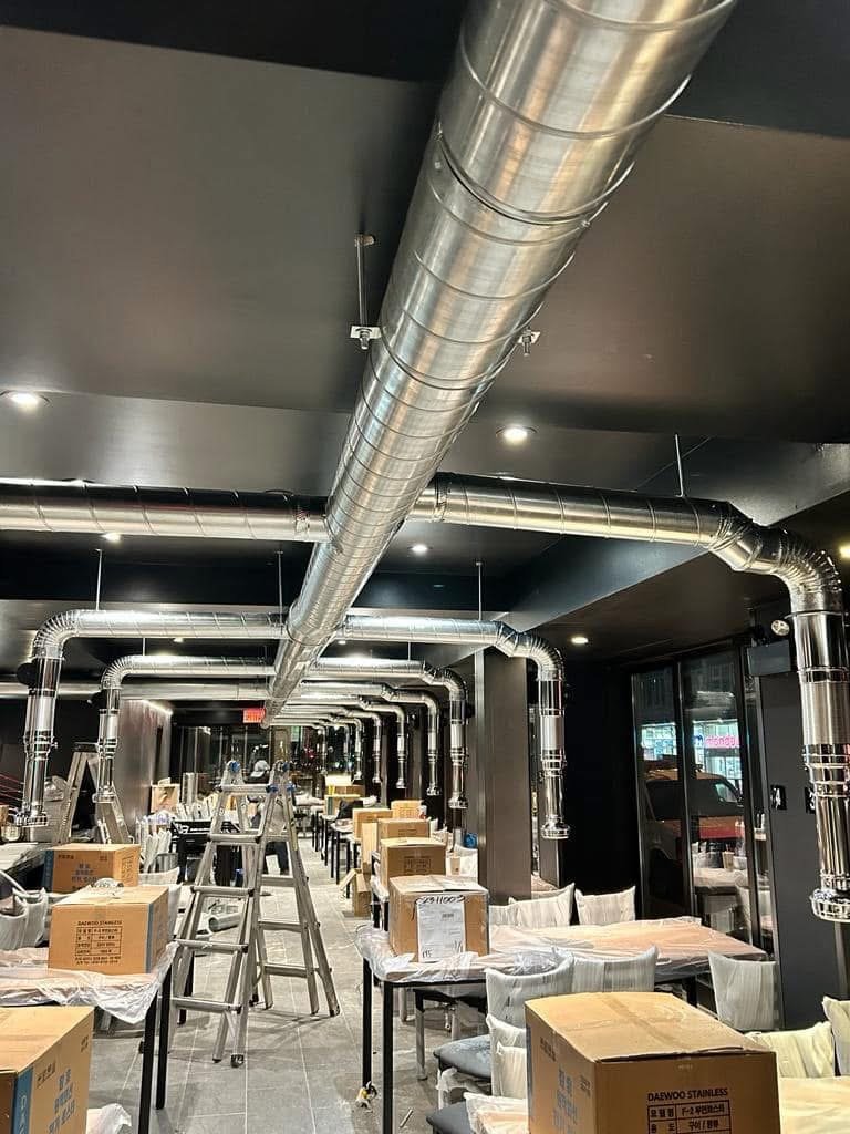Grande pièce en chantier avec des conduits métalliques de ventilation au plafond et des cartons dispersés, probablement dans un restaurant en cours de rénovation.