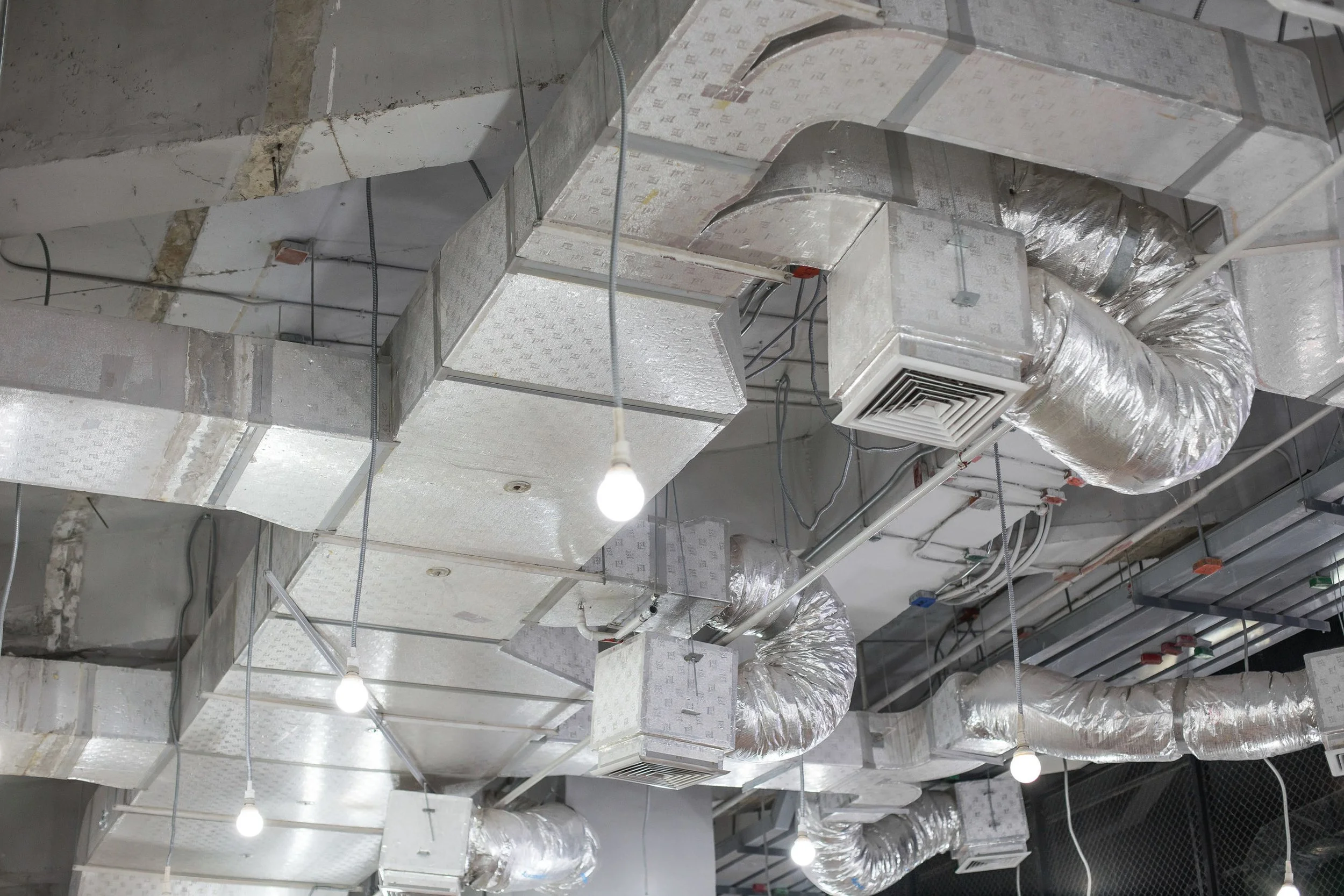 Système de ventilation industriel avec des conduits en métal et des câbles suspendus au plafond.