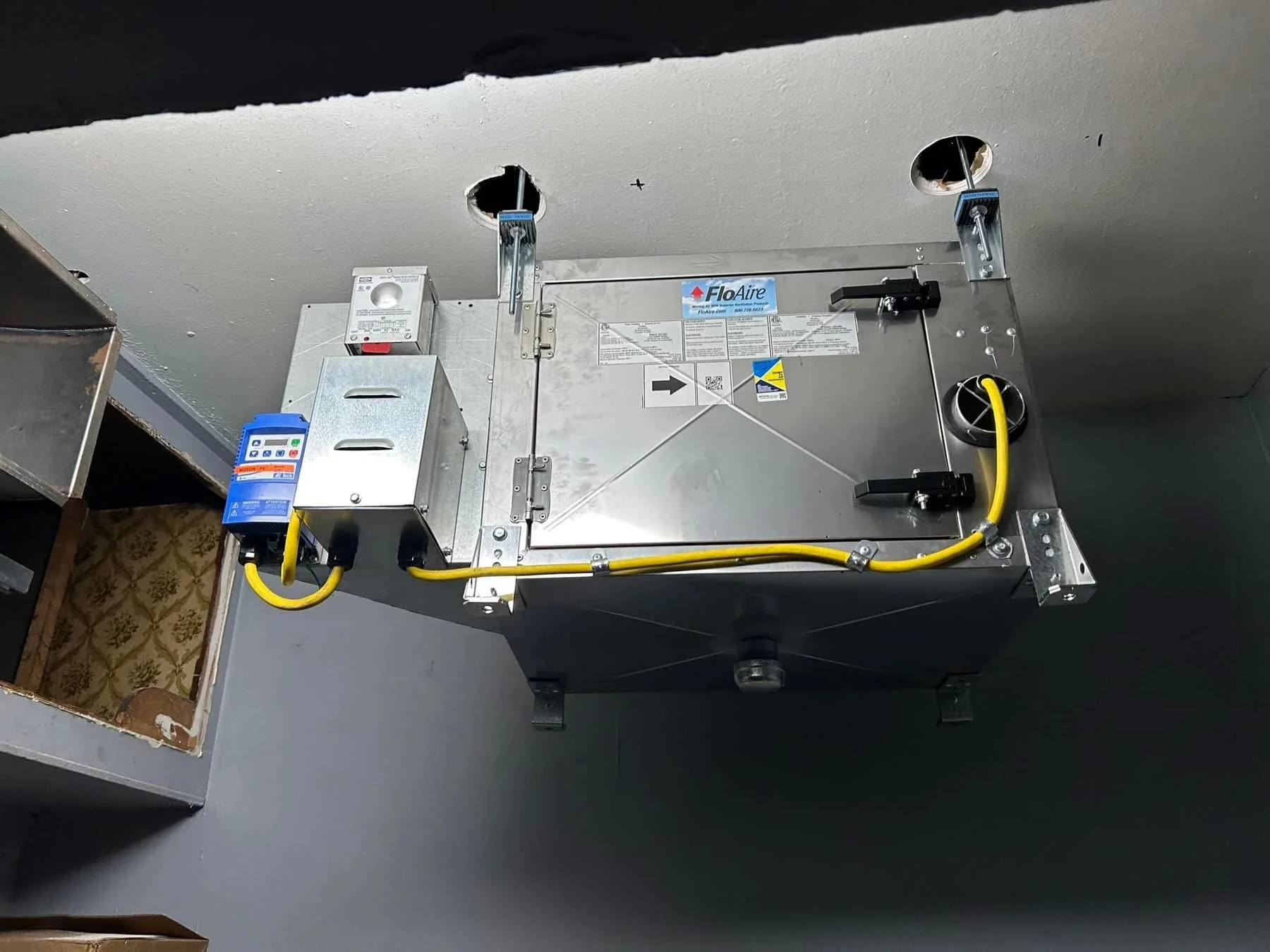 Équipement de ventilation industriel monté au plafond avec câbles jaunes et boîtier de commande.