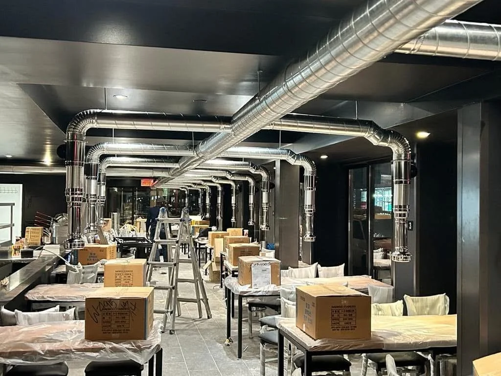 Intérieur de restaurant en construction avec tuyaux d'aération apparents, échelles et boîtes en carton.