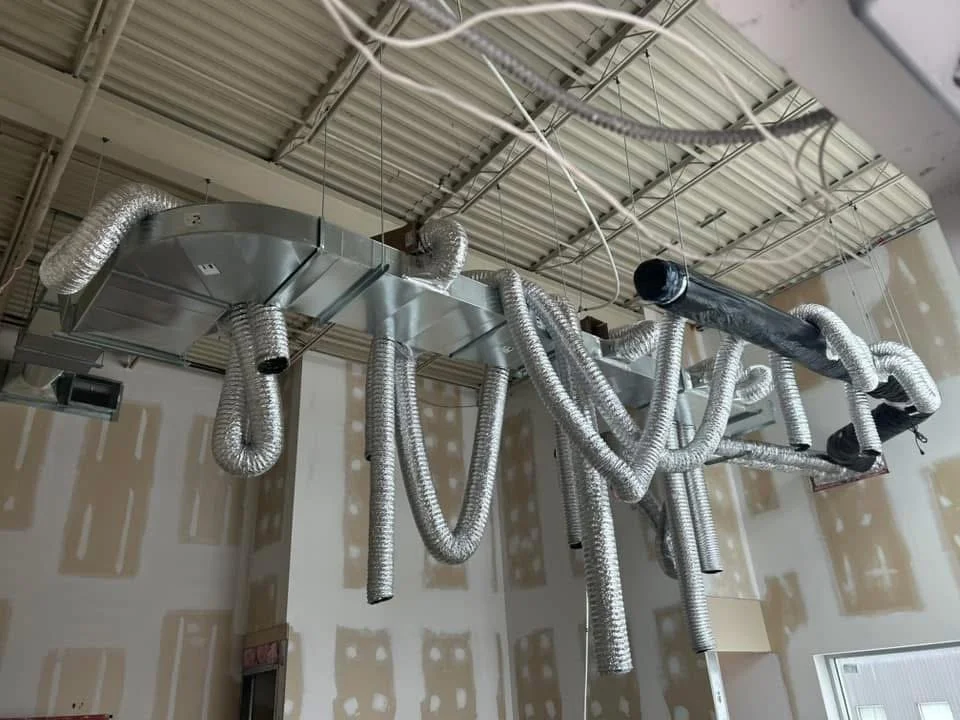 Plafond avec conduits d'air flexibles argentés suspendus dans une pièce en construction.