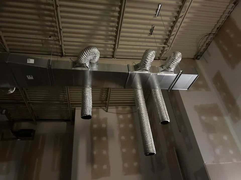 Conduits de ventilation métalliques au plafond d'un bâtiment industriel.