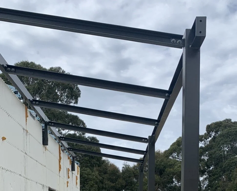 Bespoke steel verandah structure under construction outdoors with cloudy sky and native Australian trees in background.