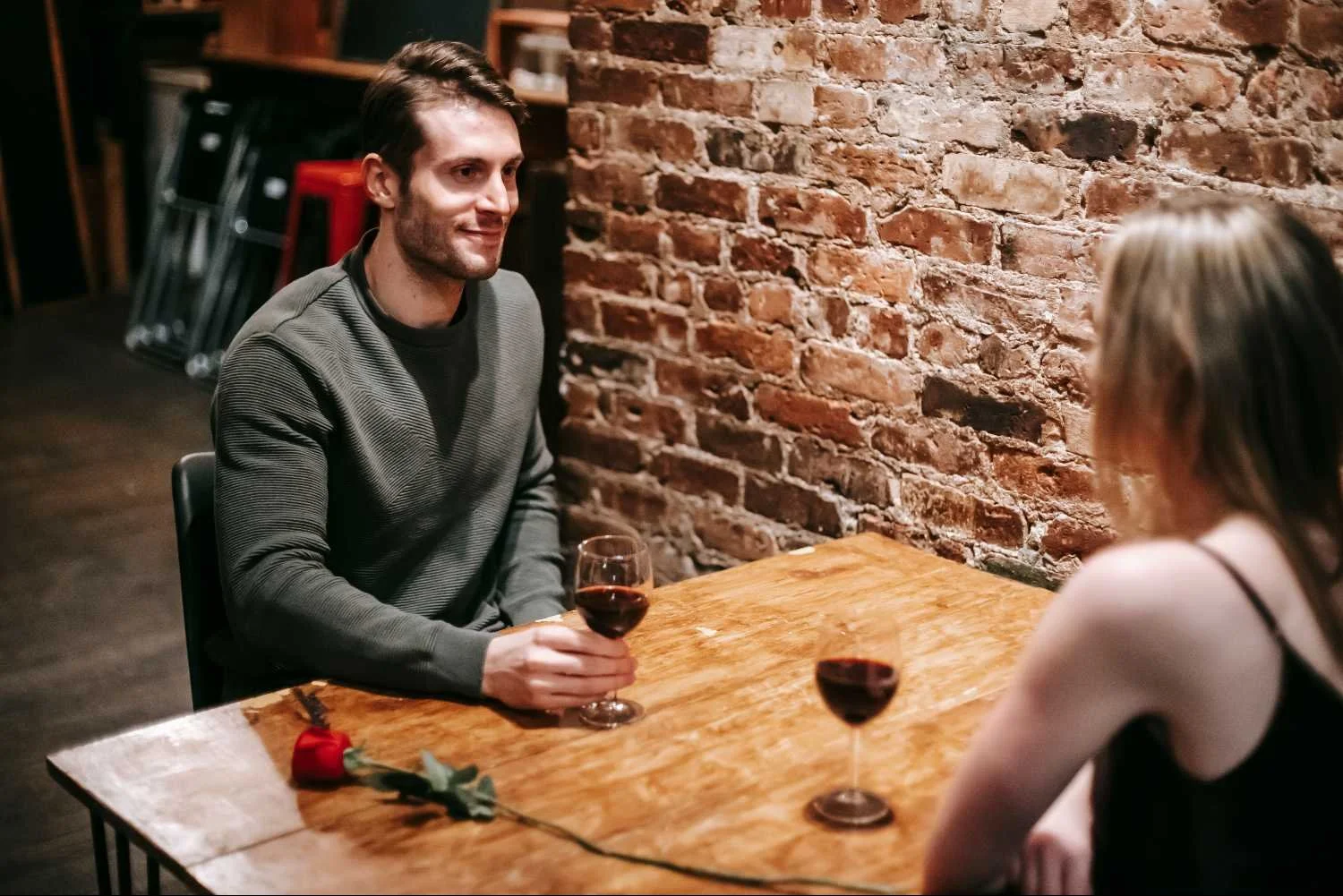 Man holding wine glass at restaurant table across from woman, illustrating secure attachment and grounded dating for men in Mooresville NC.