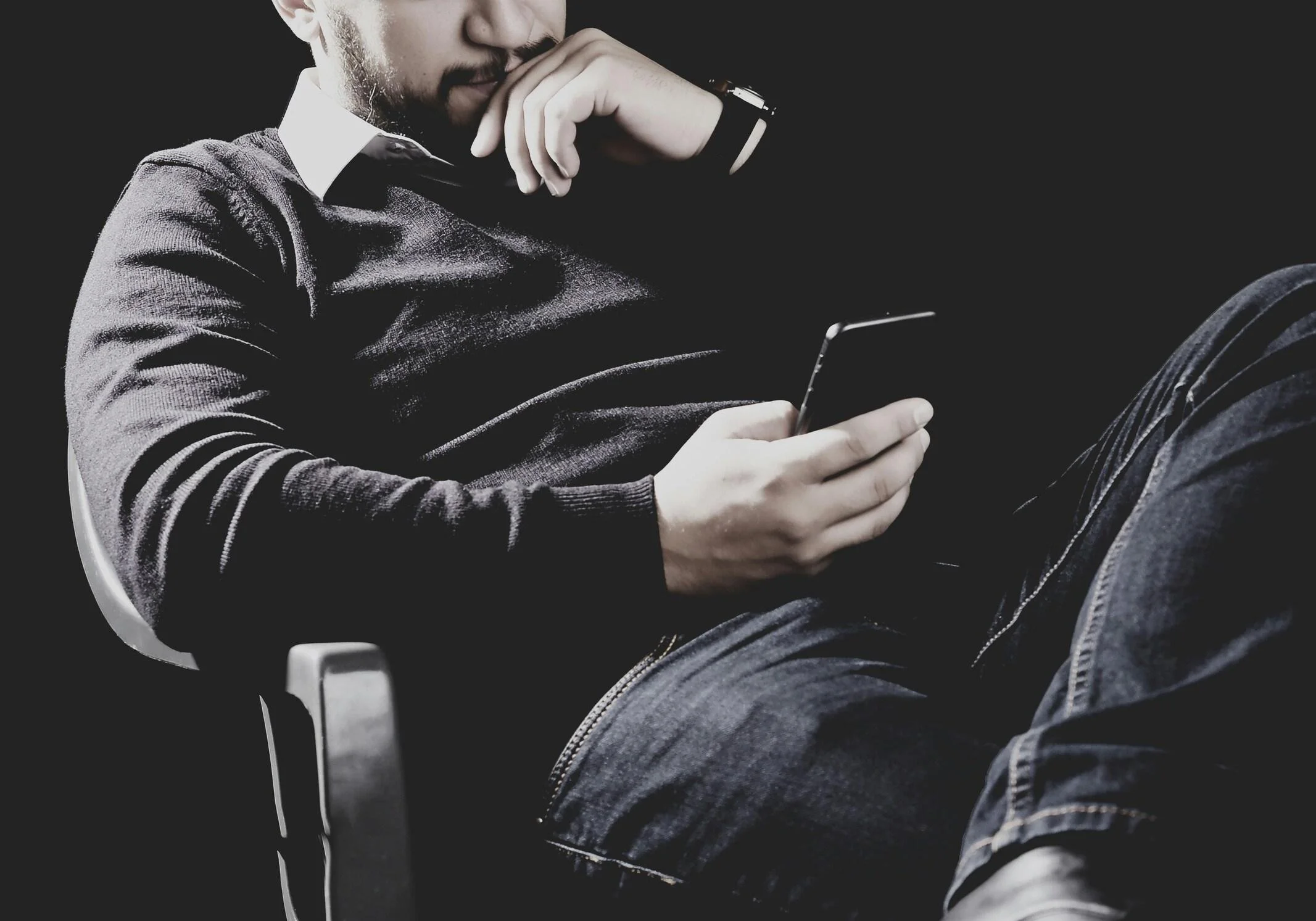 Close-up of a man in a sweater checking his phone in a dark room, representing the secrecy and shame of a habit he's carrying alone