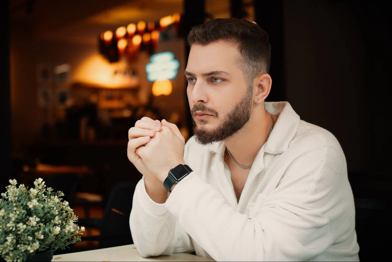 Young man seated at cafe table, hands clasped, gazing away, avoidant attachment therapy for men in Mooresville NC.