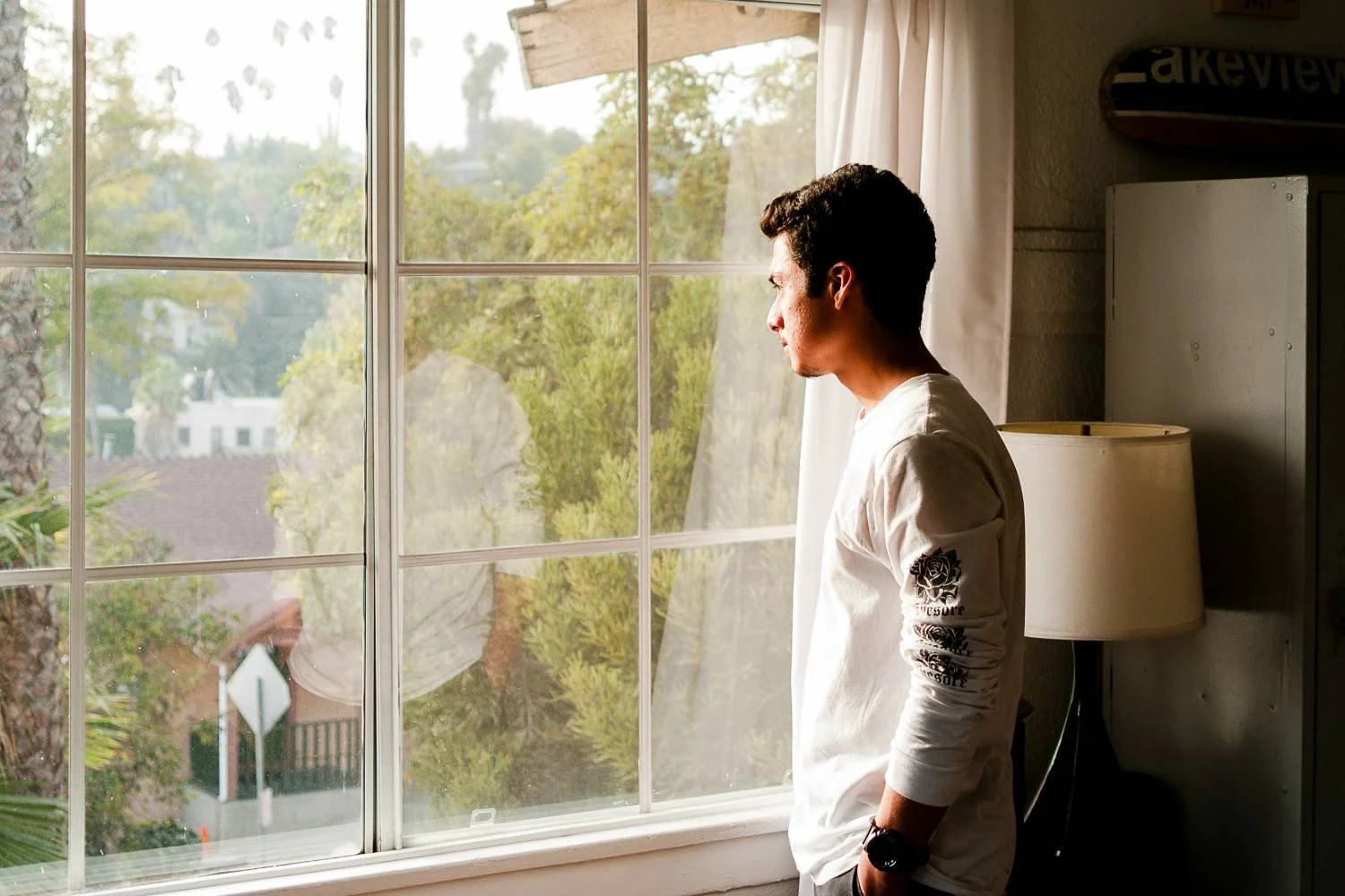 Young man standing at a window looking outside, representing clarity about a toxic relationship cycle in men's therapy.