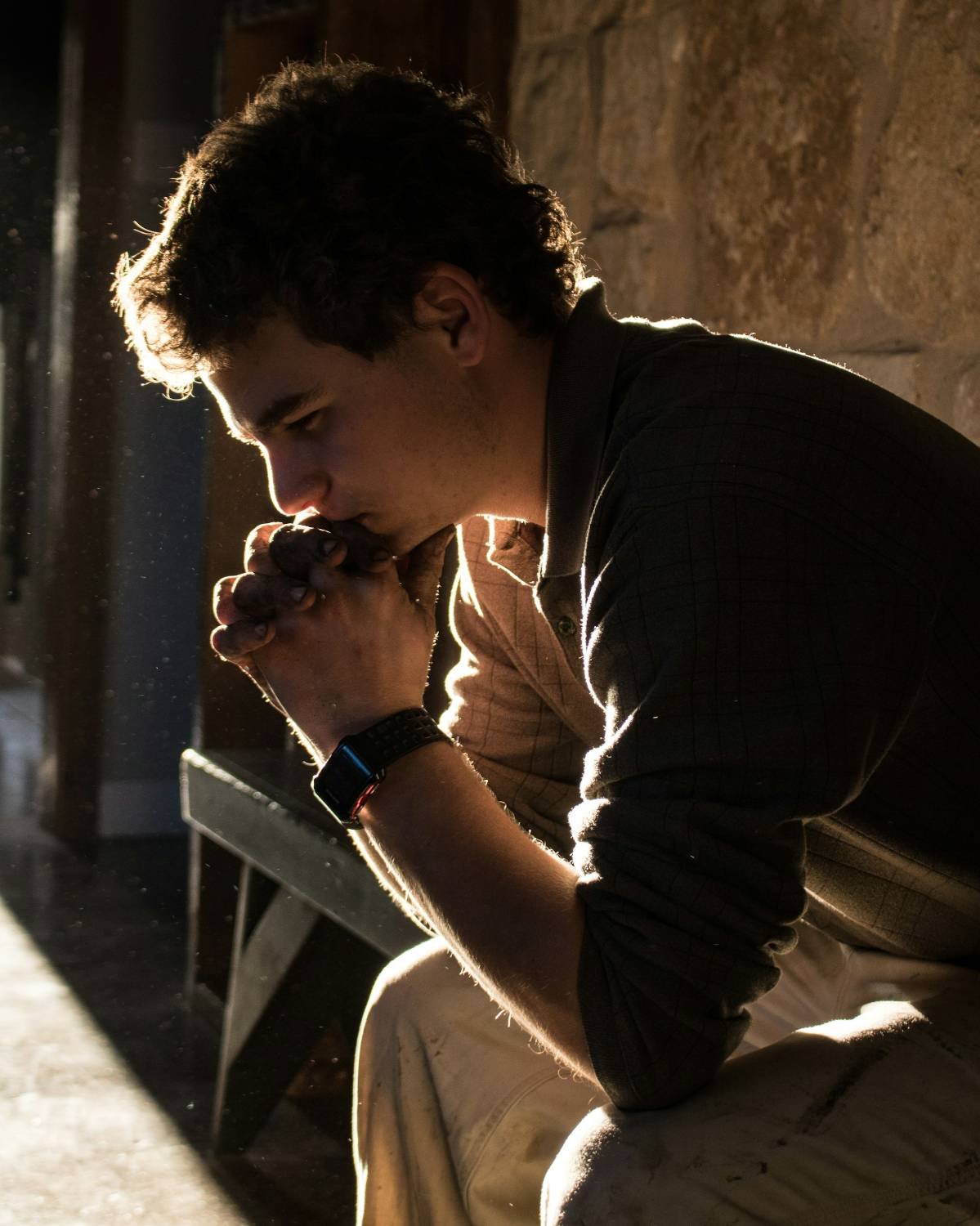 Young man seated in a stone church, hands clasped to his mouth, head bowed, related to scrupulosity and religious OCD counseling in North Carolina.
