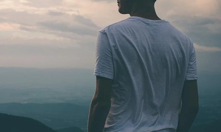 Man seen from behind at a mountain overlook, representing the clarity that opens up once a man stops repeating the same pattern and starts working through it.