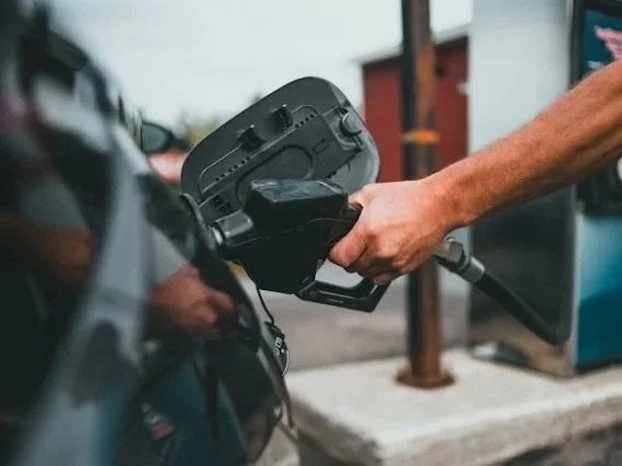 Man's hand holding a fuel nozzle inserted into a car at a gas station, representing routine autopilot behavior addressed in men's anxiety counseling.